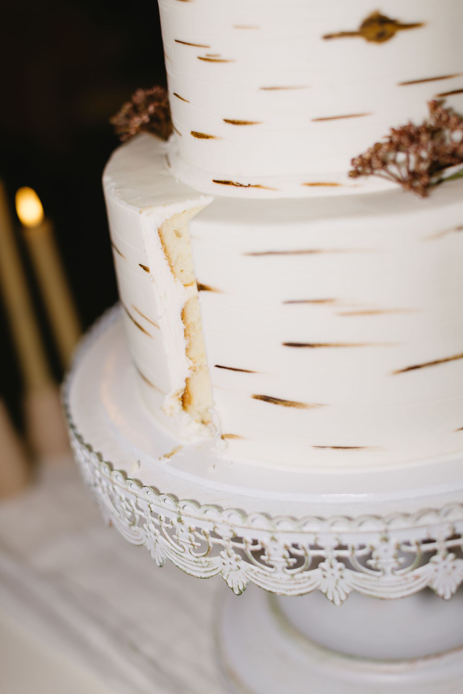 White birch-textured wedding cake with delicate lace trim on a glass cake stand.