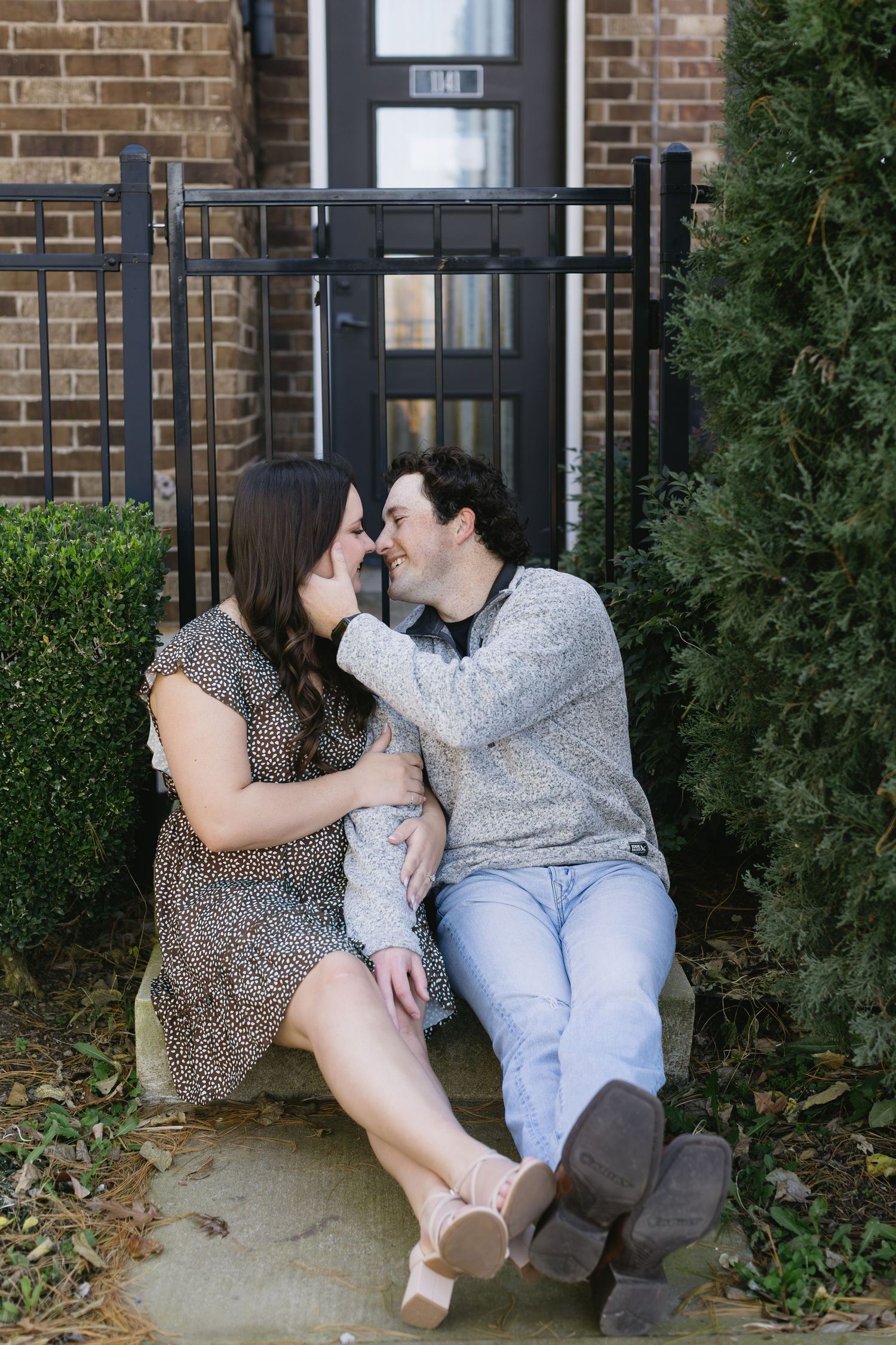 A couple shares a playful moment while sitting on steps near greenery.