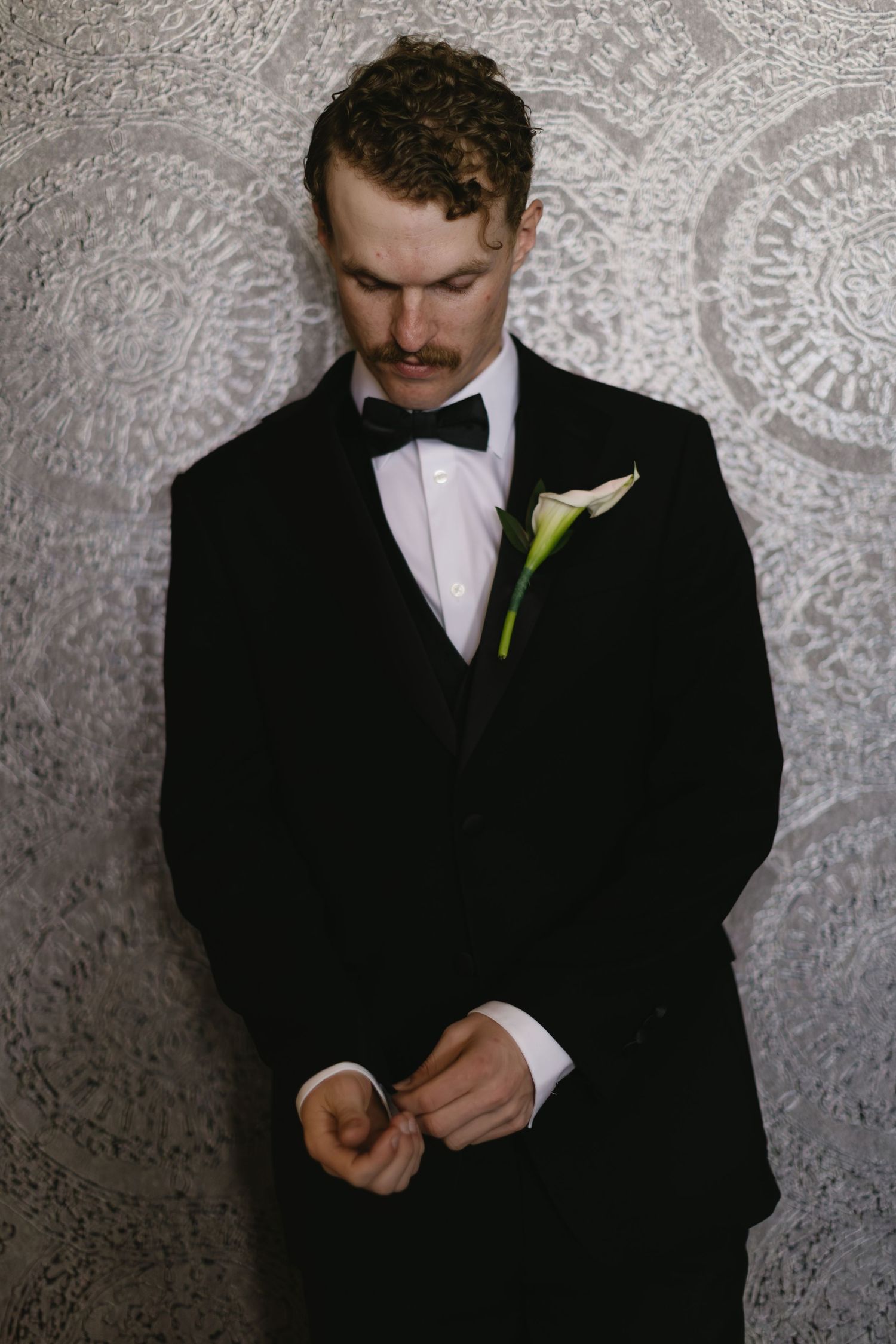Close up shots of groom adjusting bowtie and suit with green boutonniere.
