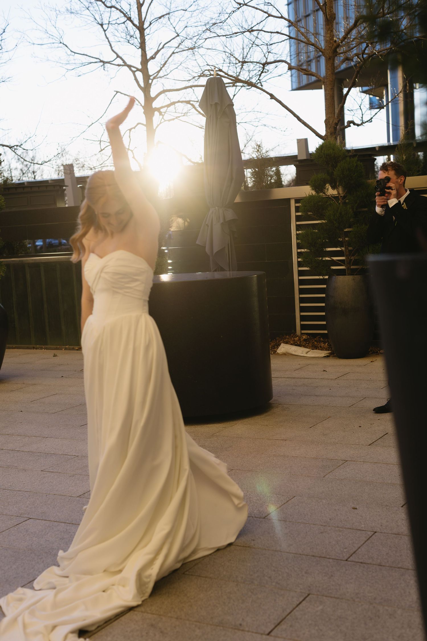 A bride in a flowing white gown twirls on a sunlit outdoor patio during golden hour.