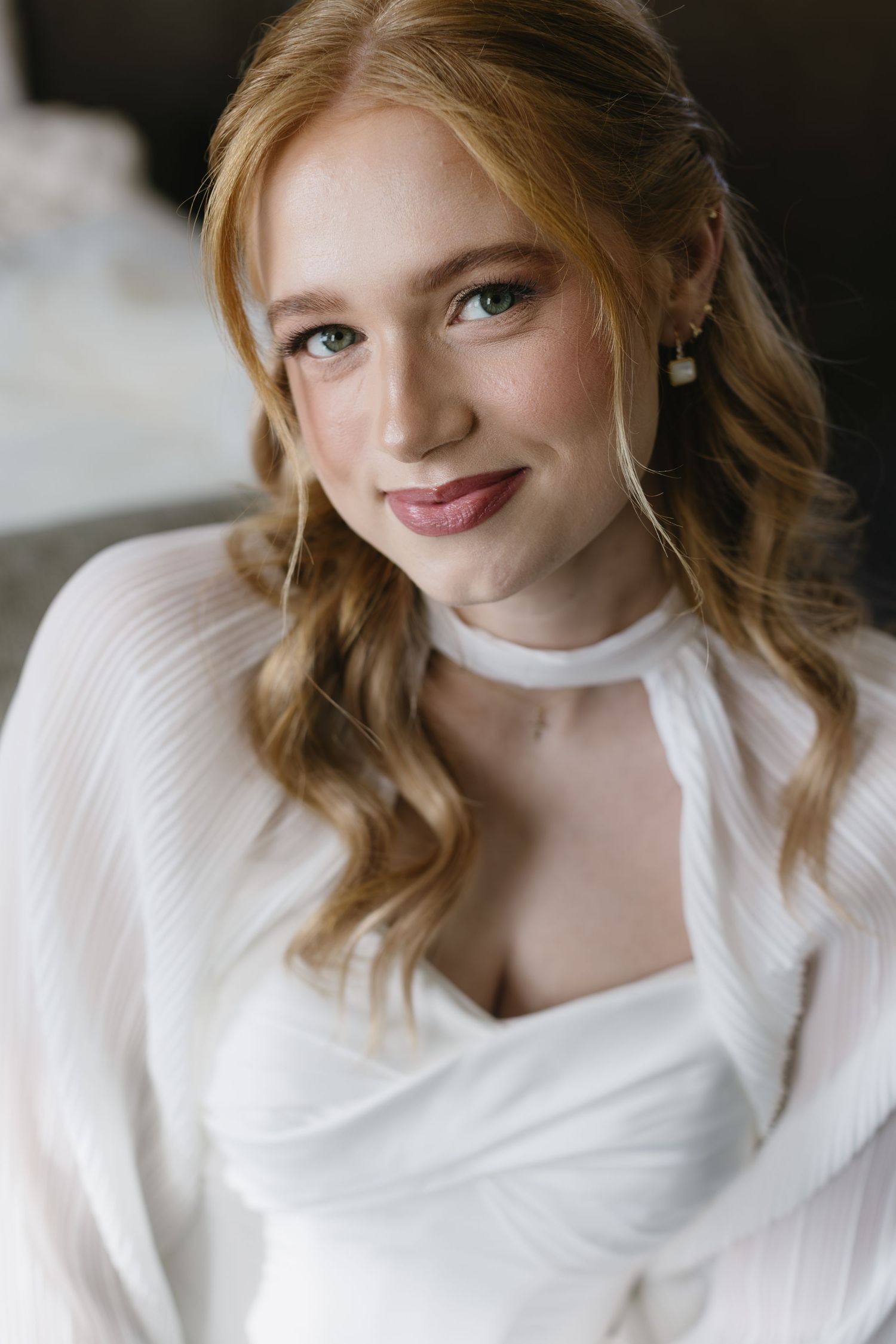 A bride wearing a classic white dress smiles warmly in an indoor portrait session.
