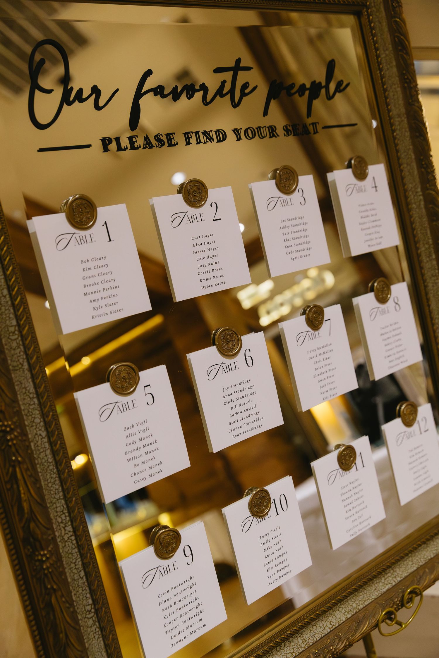 An elegant mirror frame displays wedding seating assignments with gold wax seals.