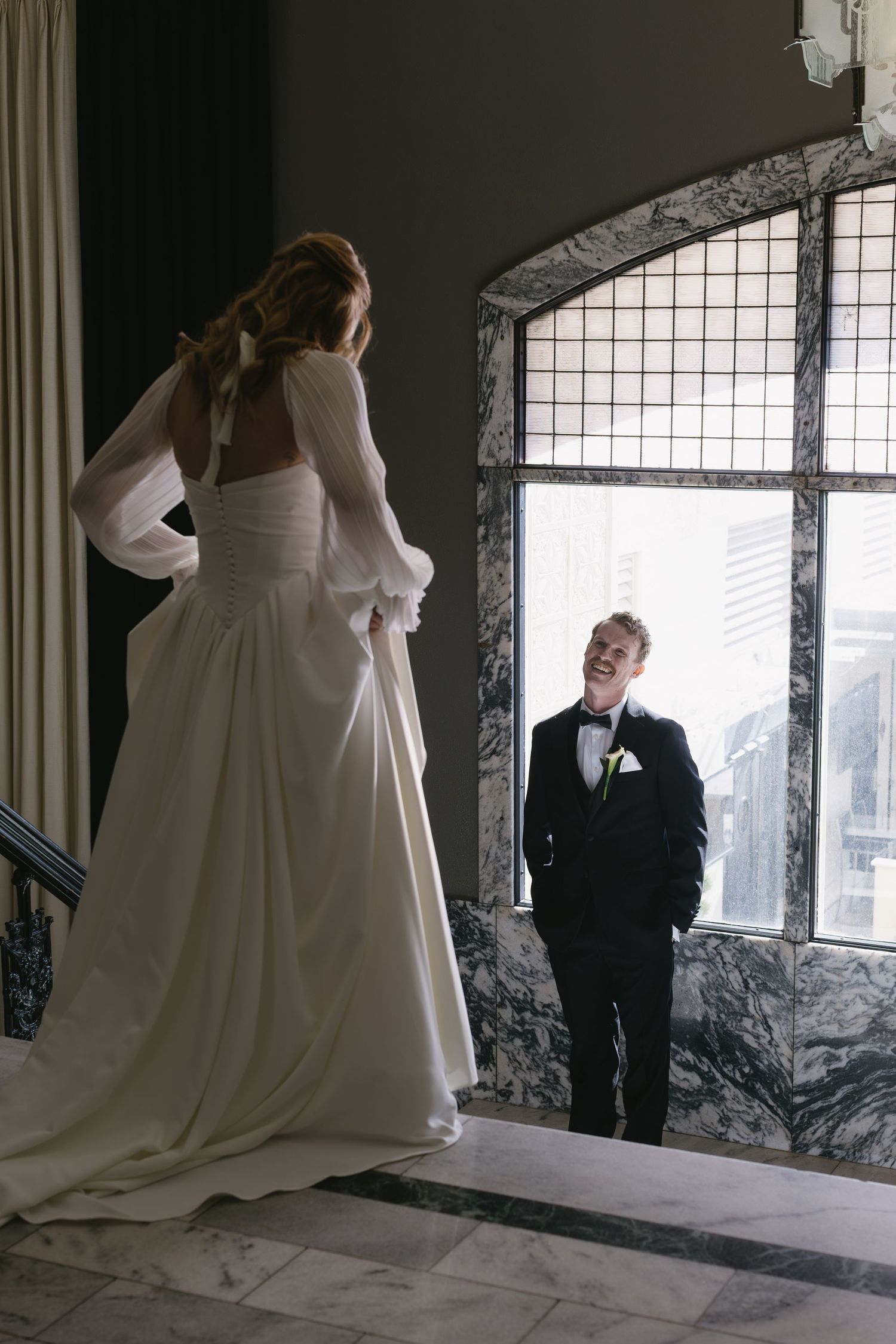 Artistic wedding portraits taken in front of a stone window with natural light streaming in.