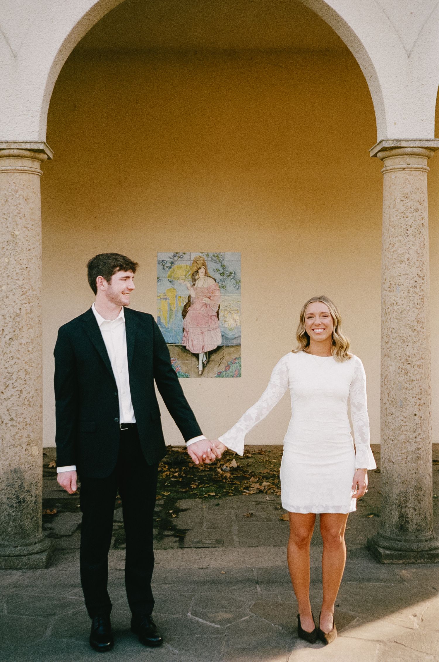 A couple posing playfully under architectural arches with cream-colored walls.
