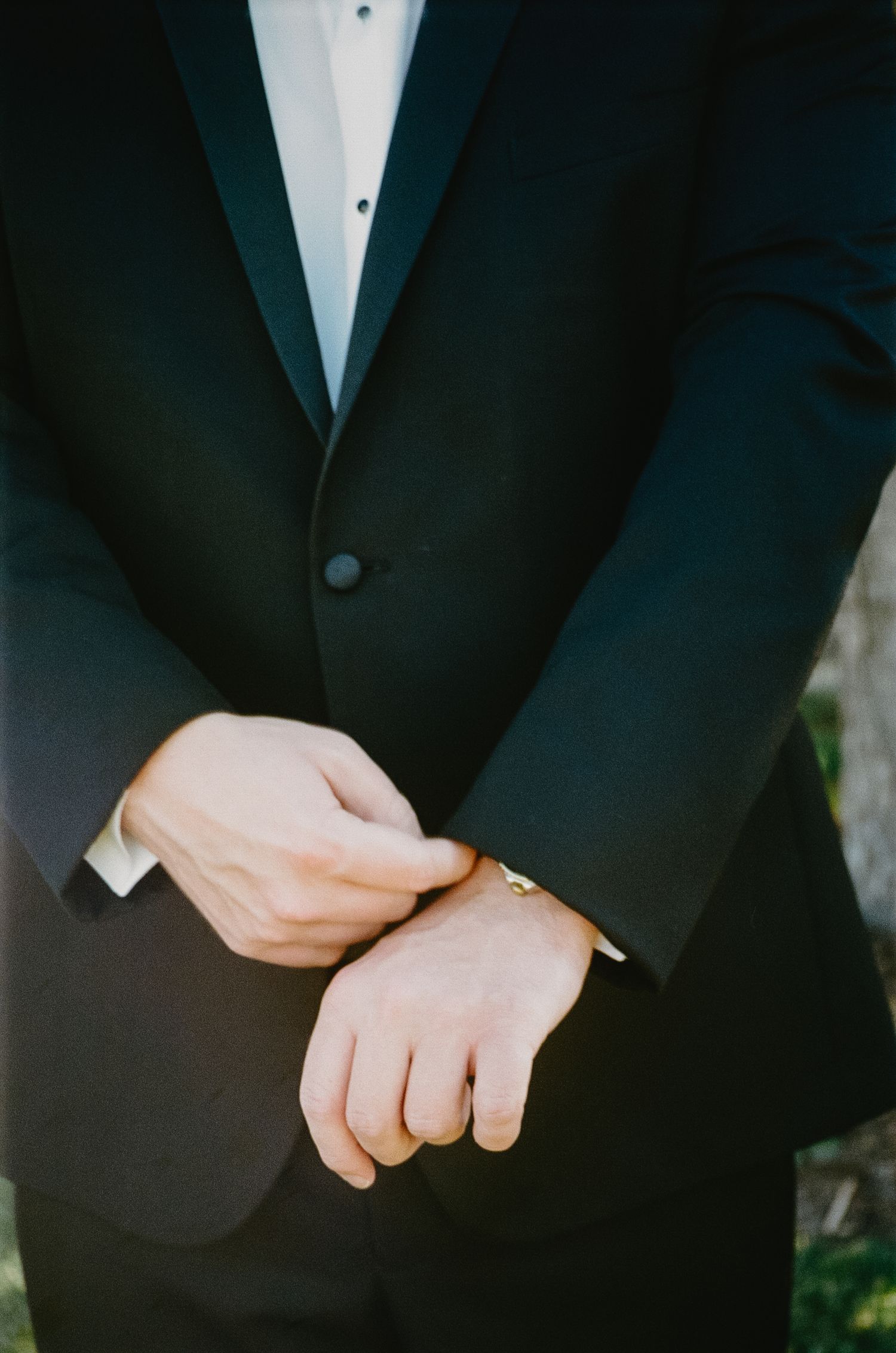 Detail shot of groom's hands with wedding ring and black tuxedo jacket.