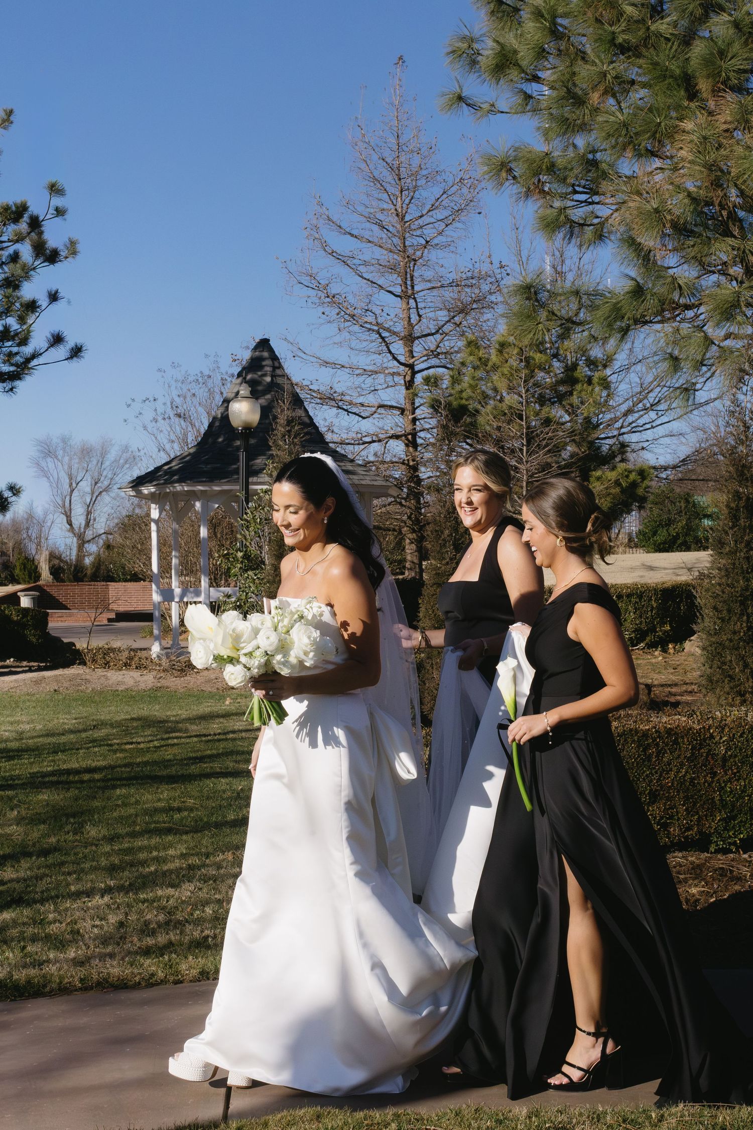 Wedding party walking outdoors with bridesmaids in black dresses and white bouquets.