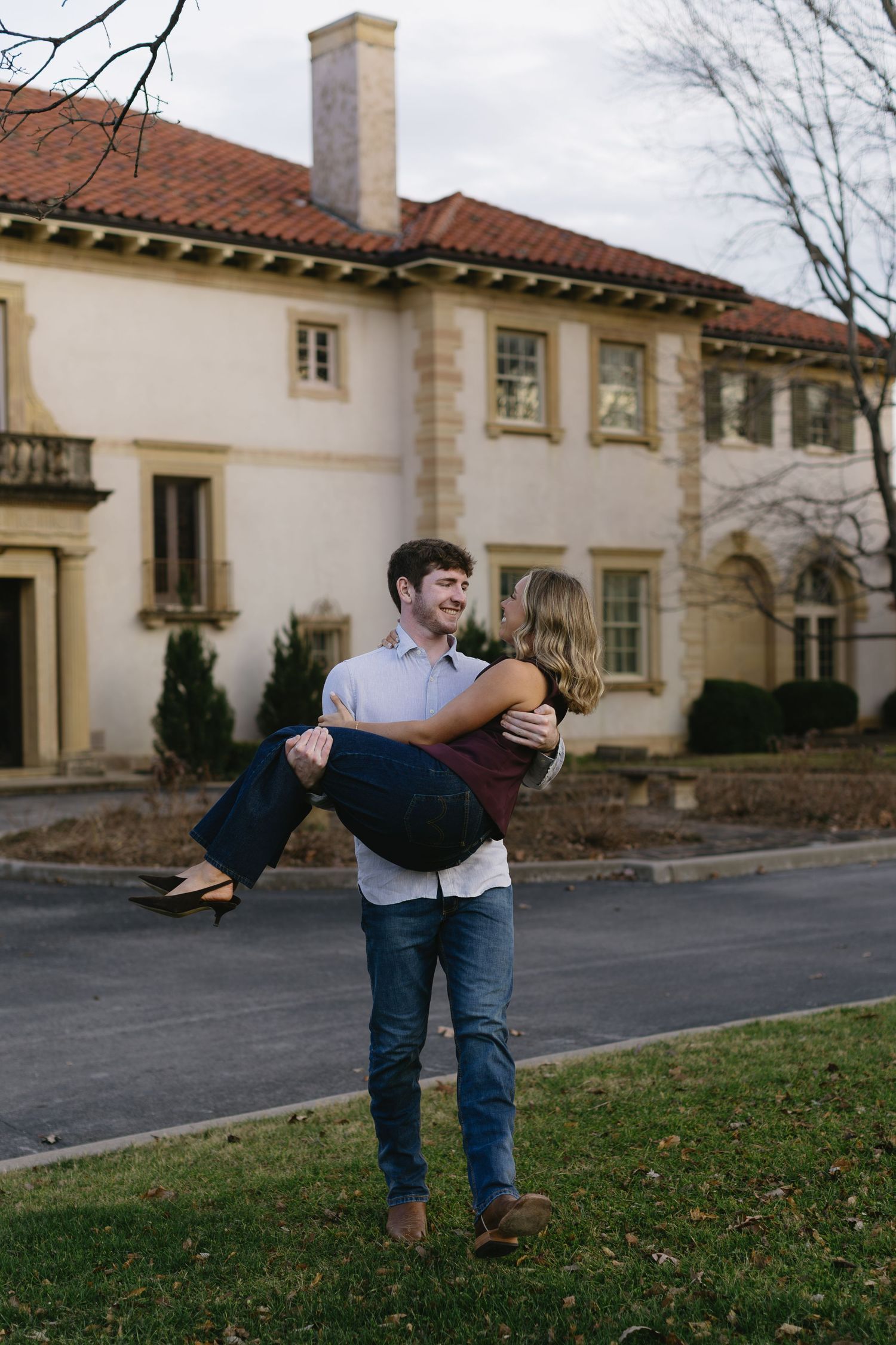 A couple shares a playful dance move on the lawn of a Mediterranean-style building.