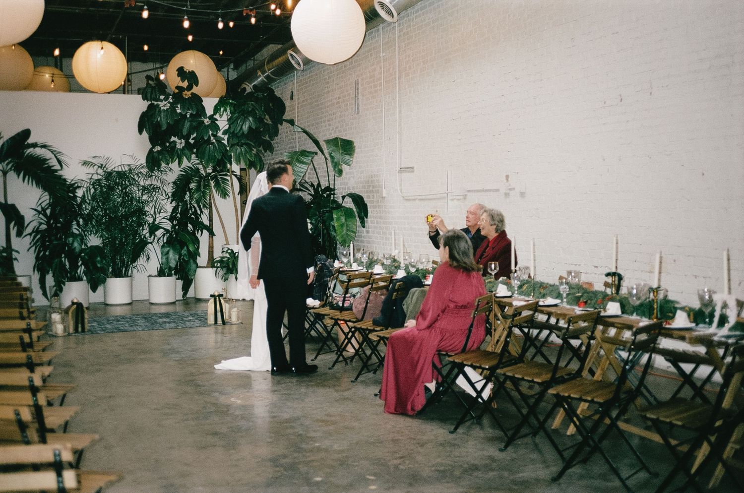 Wedding reception venue with string lights, potted plants, and director-style chairs.