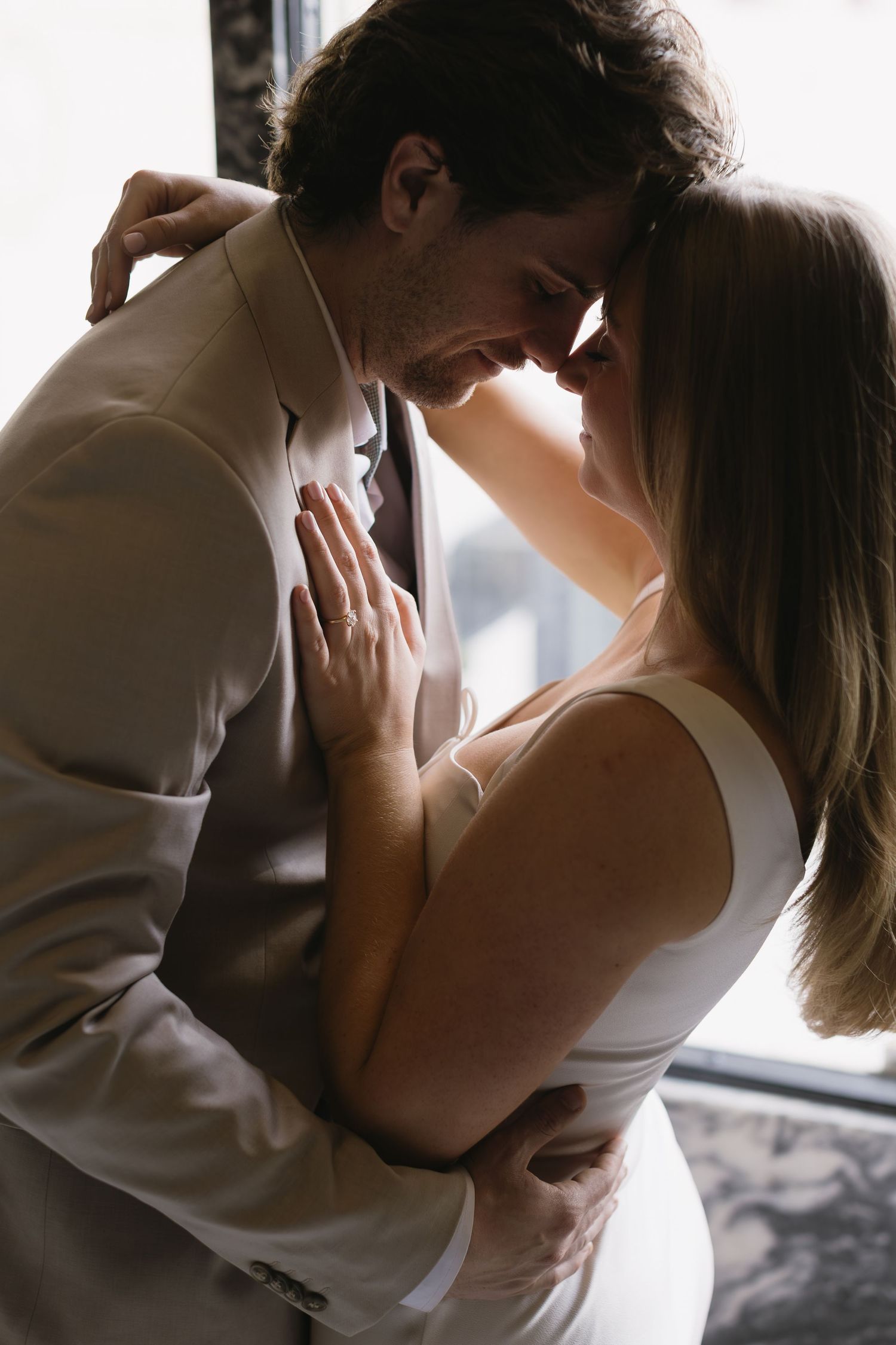 An intimate moment between a couple in light-colored formal wear sharing a tender embrace.