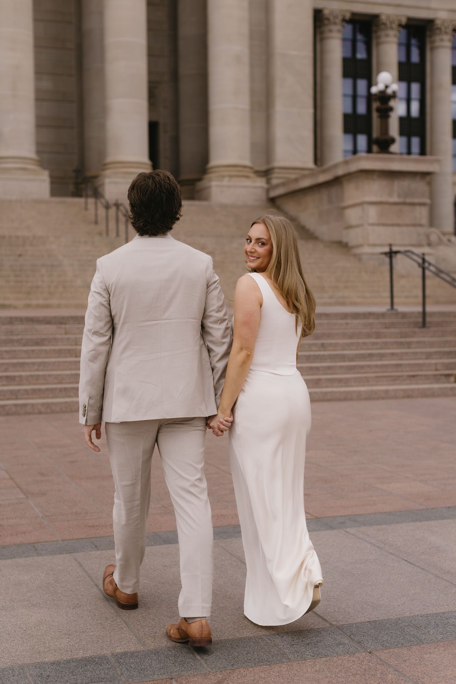 Couple in matching light colored outfits walking up stone steps of a grand building.