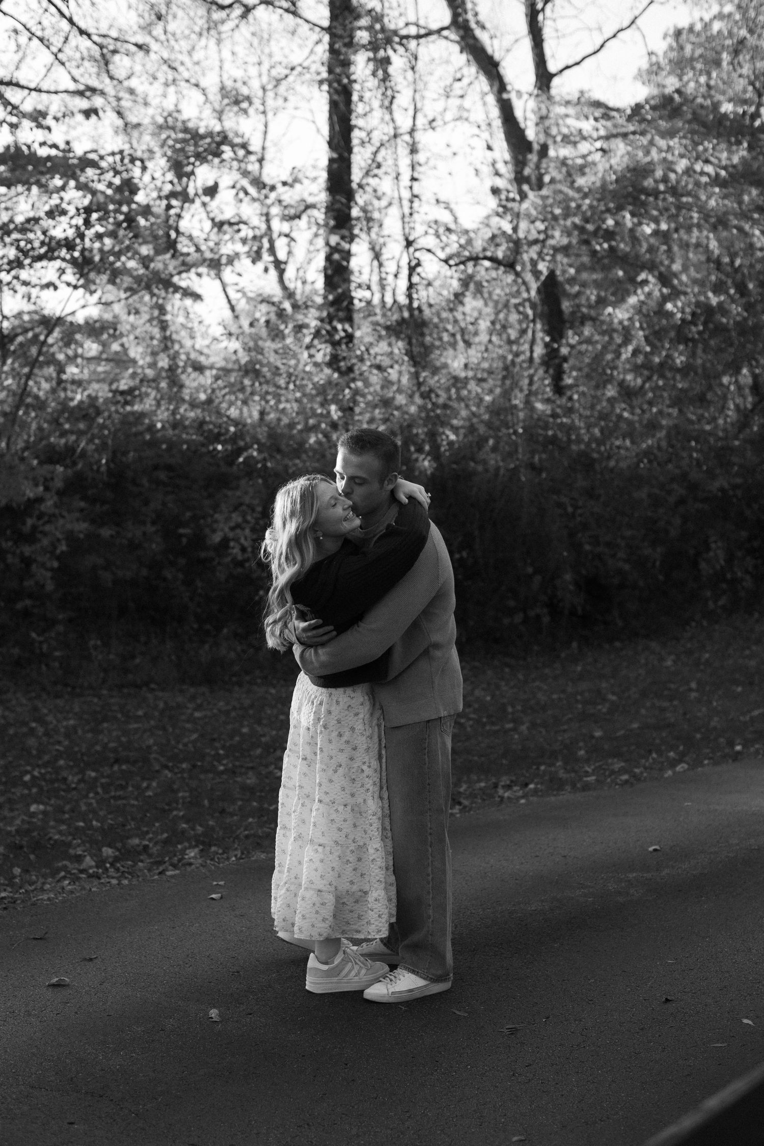 A couple embraces on a tree-lined path during an autumn photoshoot.