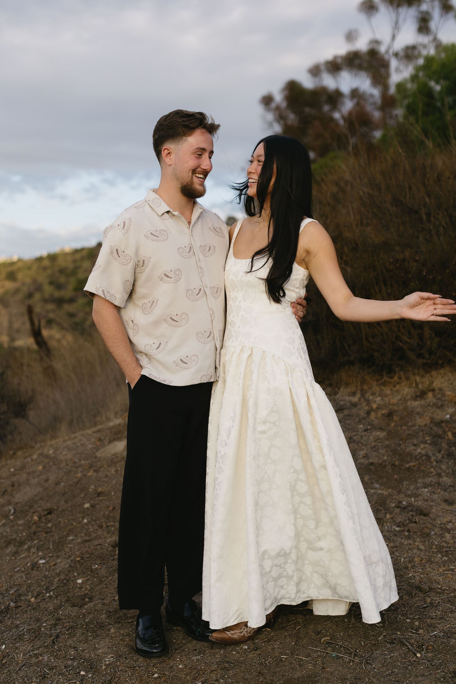 Couple in coordinating outfits share a joyful moment on a hilltop at sunset.