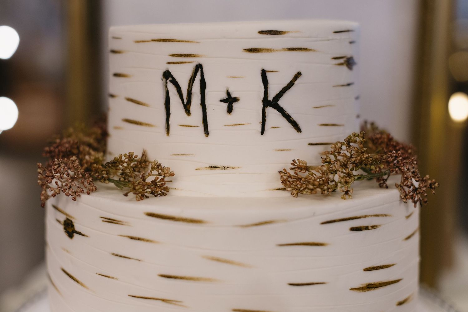 Close-up of a white wedding cake decorated with birch bark texture and gold accents.