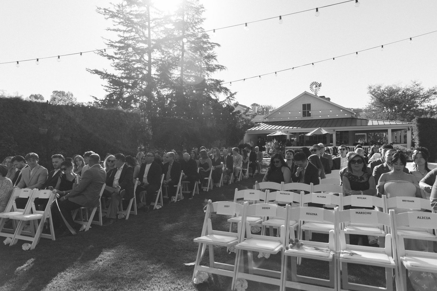 Outdoor wedding ceremony setup with white chairs and string lights under open sky.