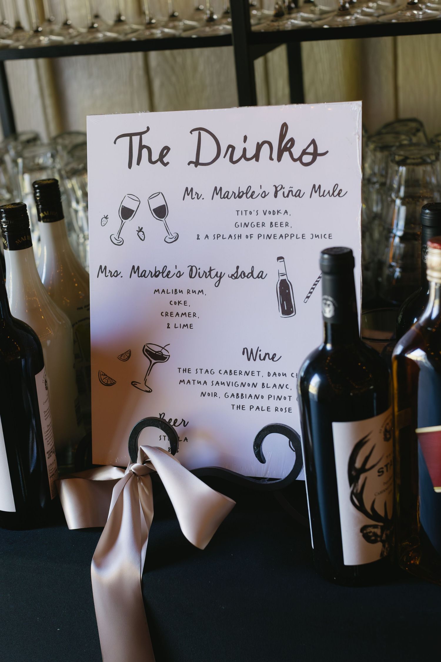 Wedding drink menu display featuring wine bottles and handwritten beverage signs.