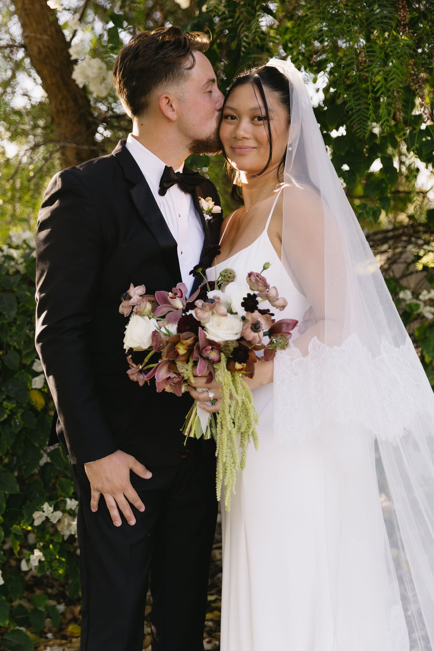 Romantic wedding couple shares intimate moment with pink and white bouquet in garden setting.