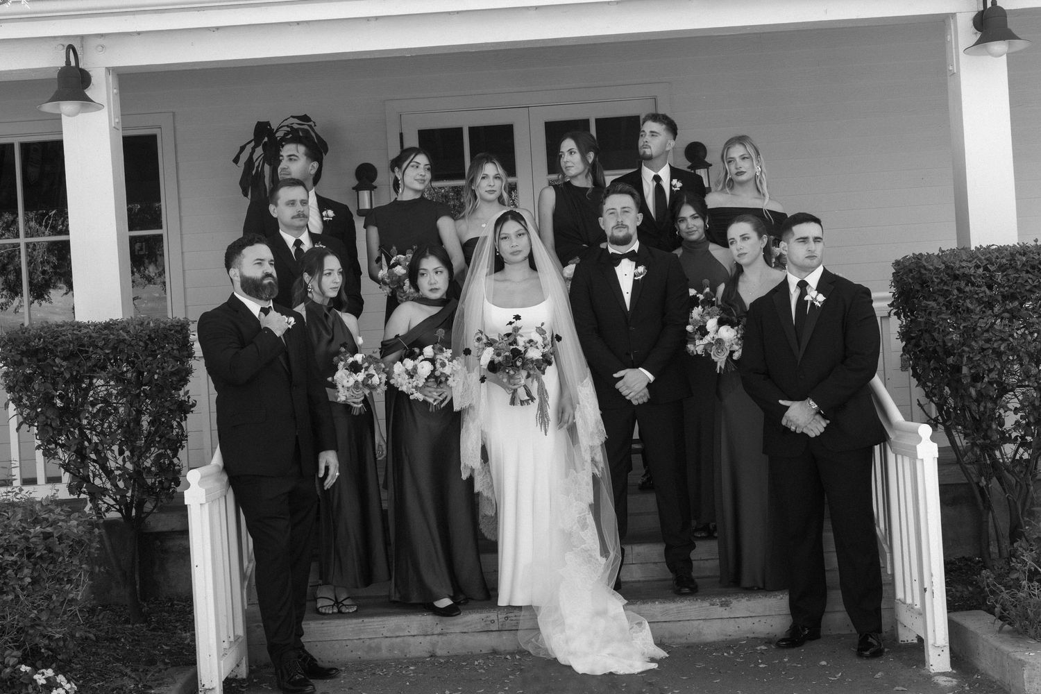 Large wedding party poses for a panoramic black and white photo on building steps.