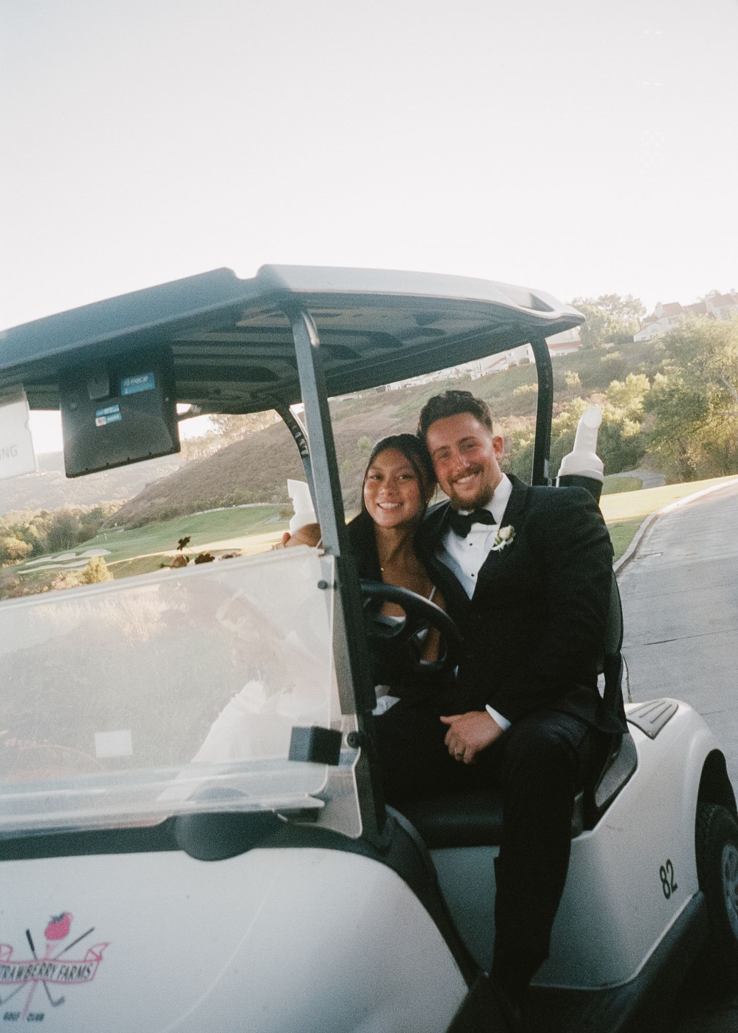 Wedding party riding in a white golf cart through a scenic outdoor venue.