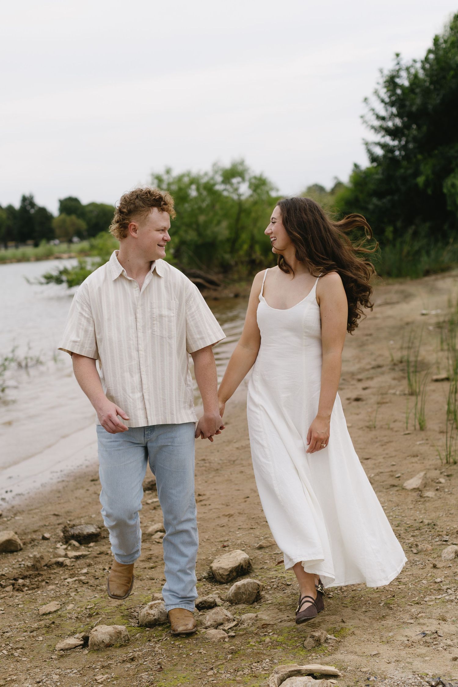 A couple strolls hand in hand along a beach path wearing coordinated casual outfits.