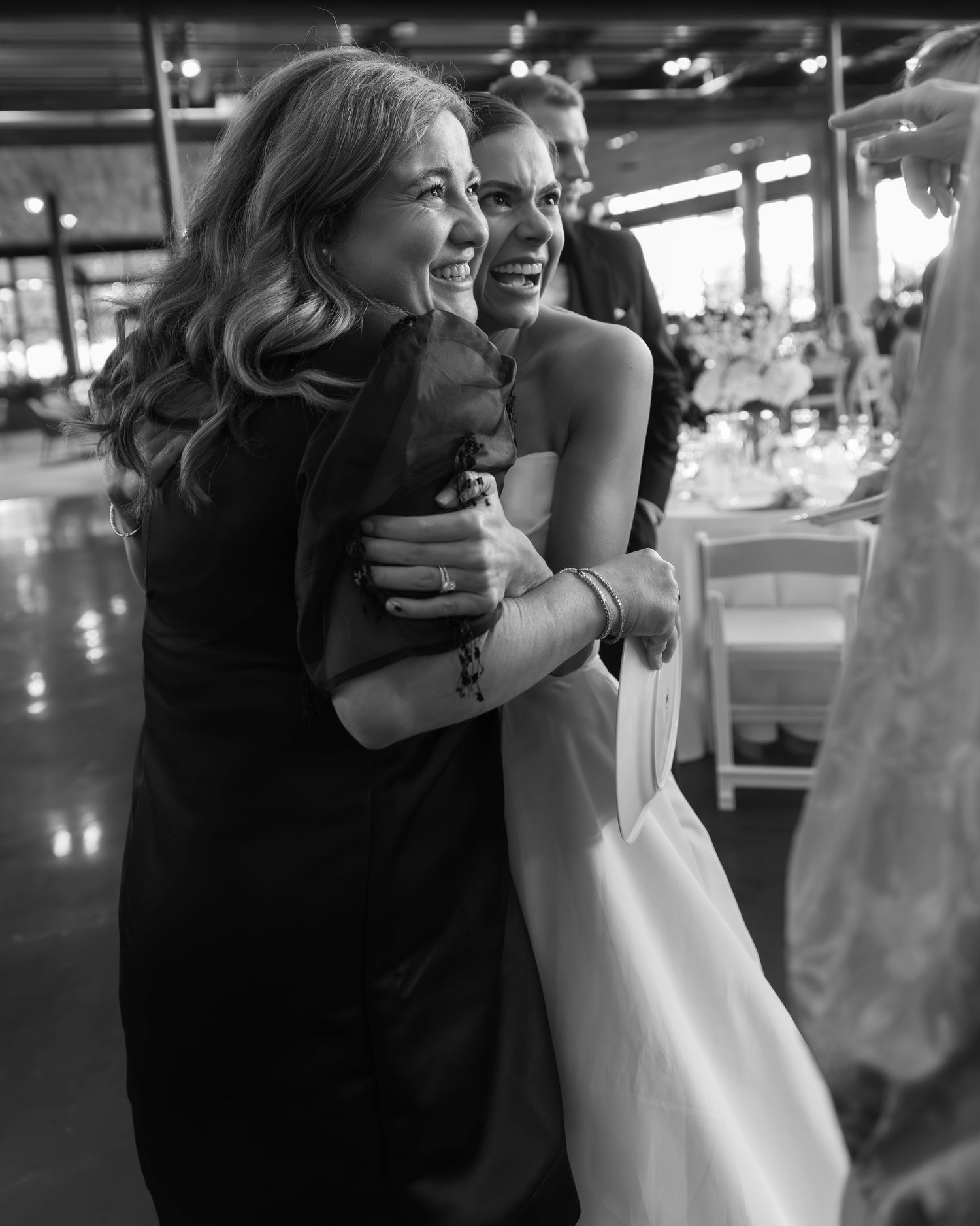 Black and white candid moment showing joyful embrace at a wedding reception.