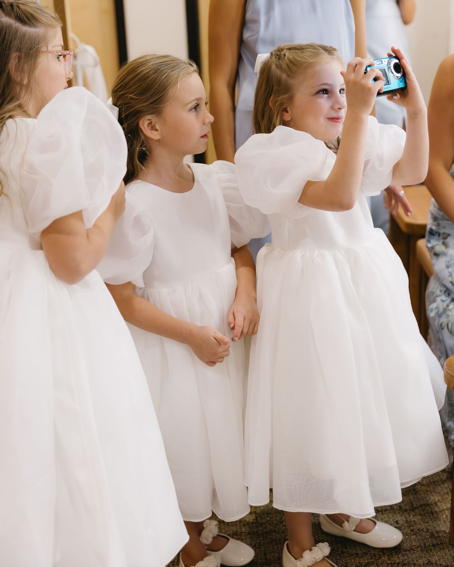 Row of young flower girls in white dresses lined up during wedding preparations.