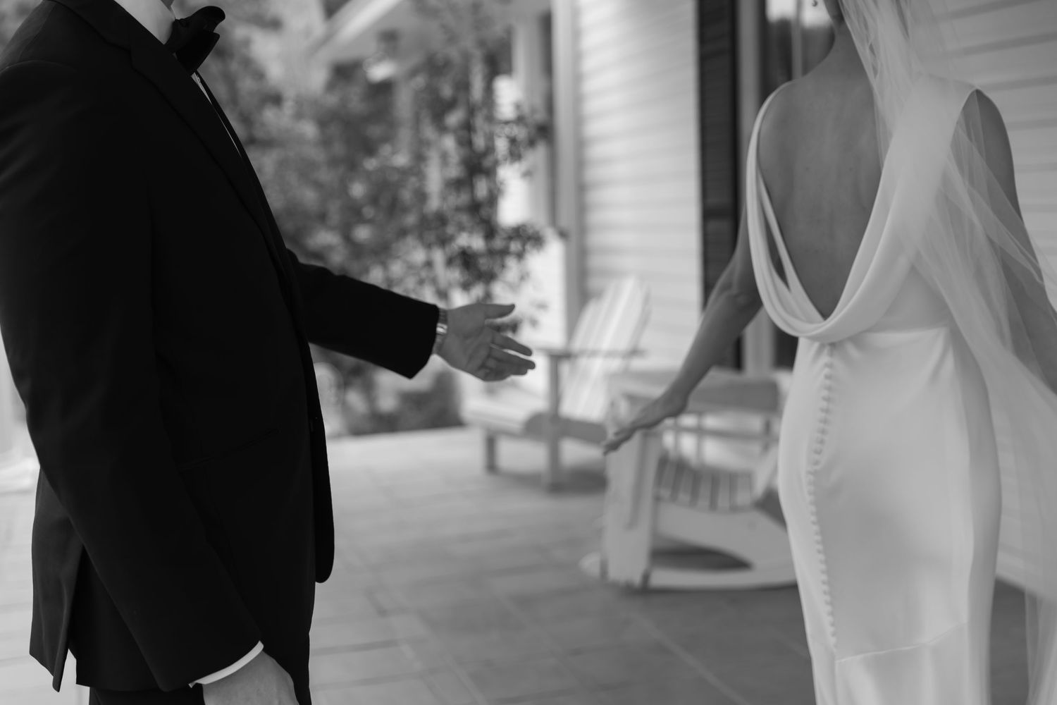 A couple in wedding attire walks down a covered outdoor pathway while attendants assist with the bride's gown.