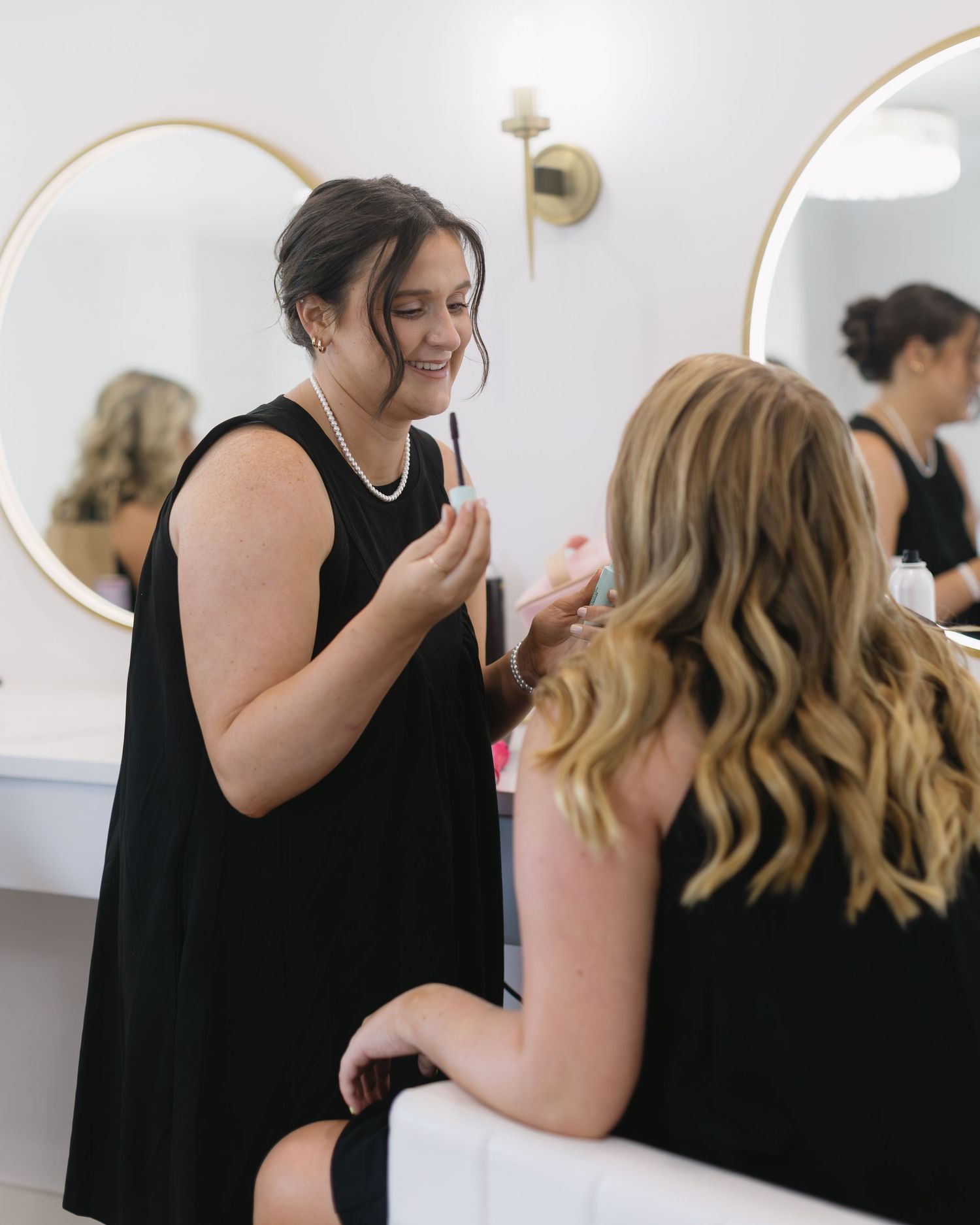 Bridesmaids in black dresses share a tender moment during wedding day preparations.
