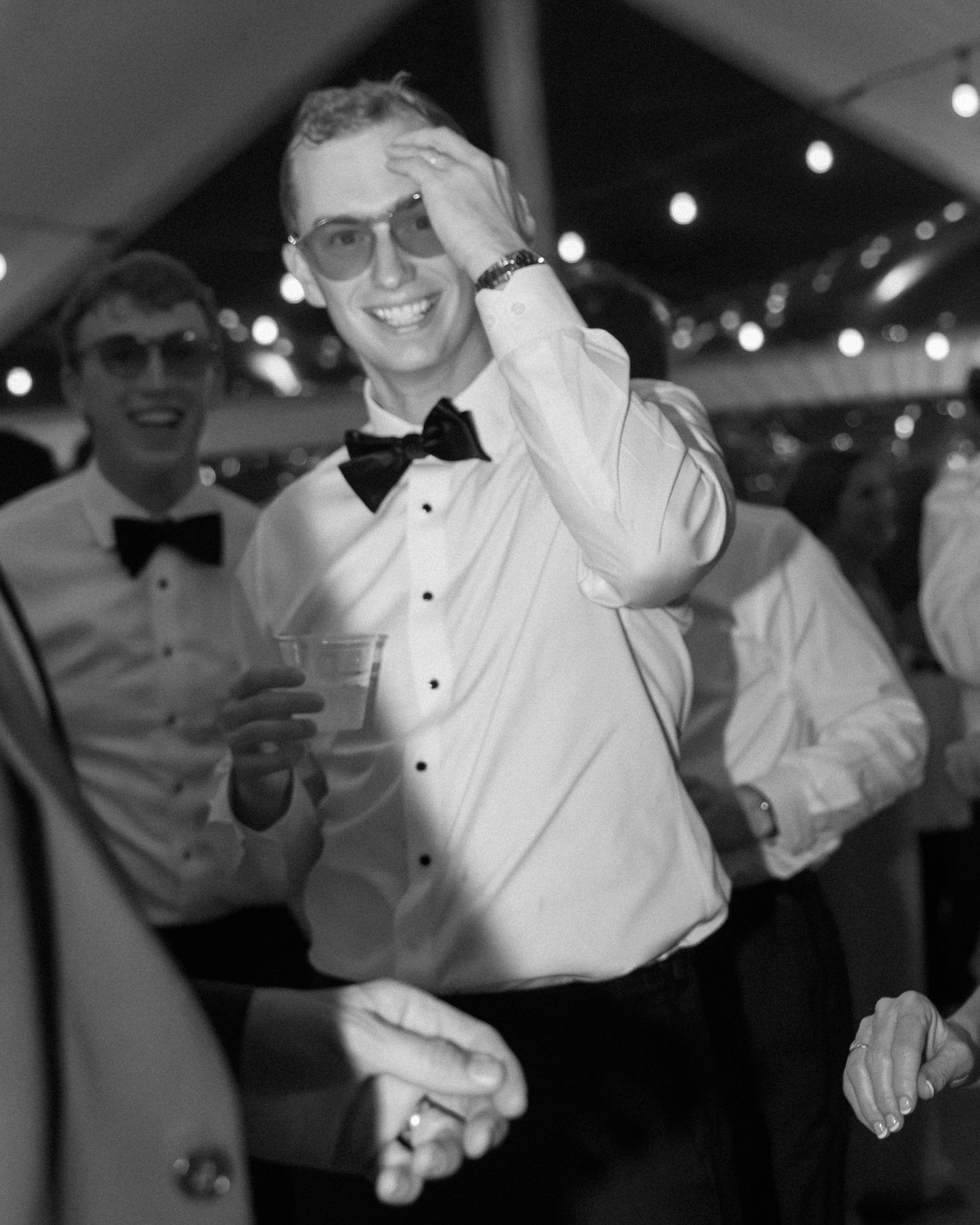 Black and white photo of guests dancing and celebrating at a formal event with string lights.