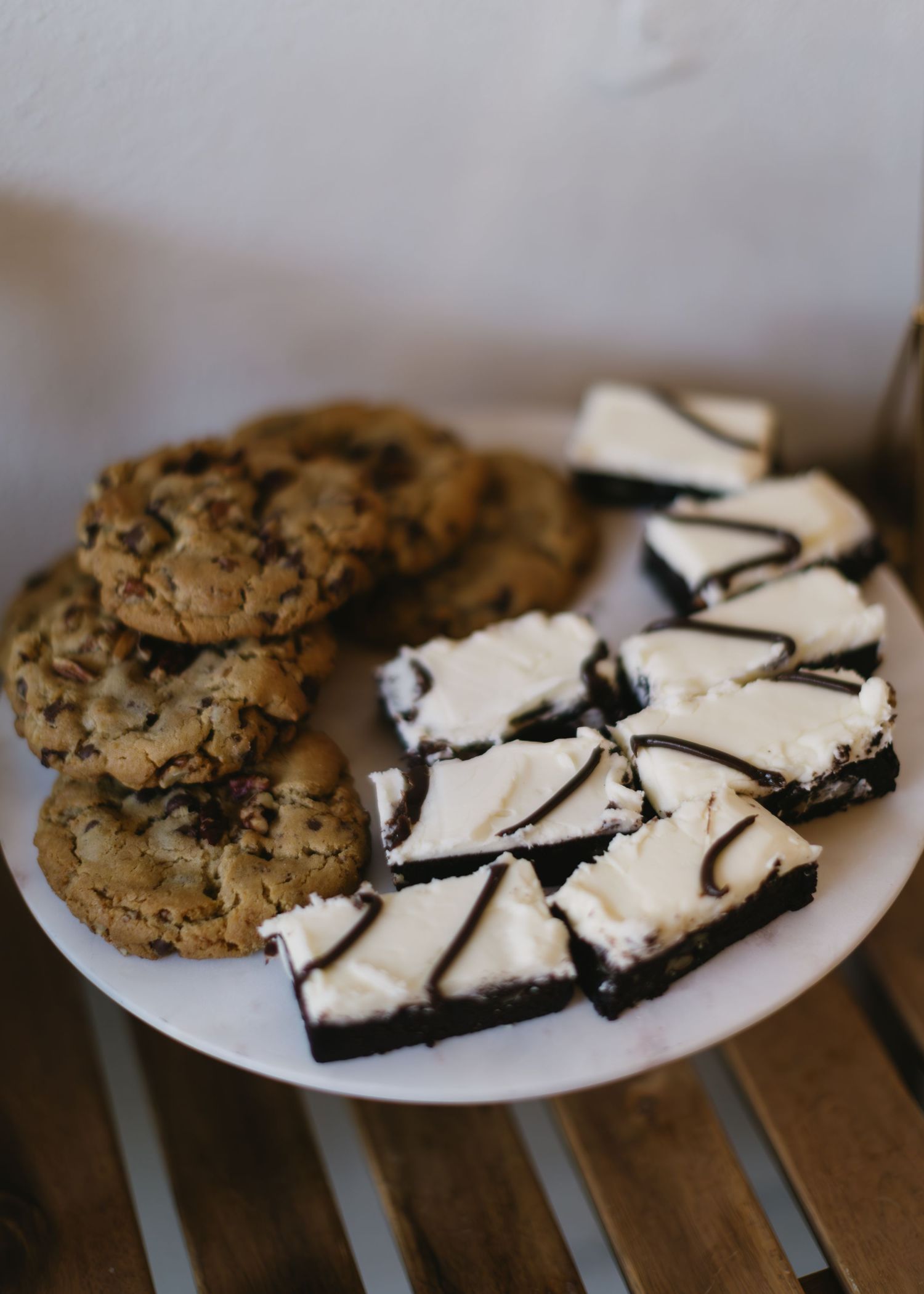 Plate of chocolate chip cookies and black and white dessert bars served on wooden surface.