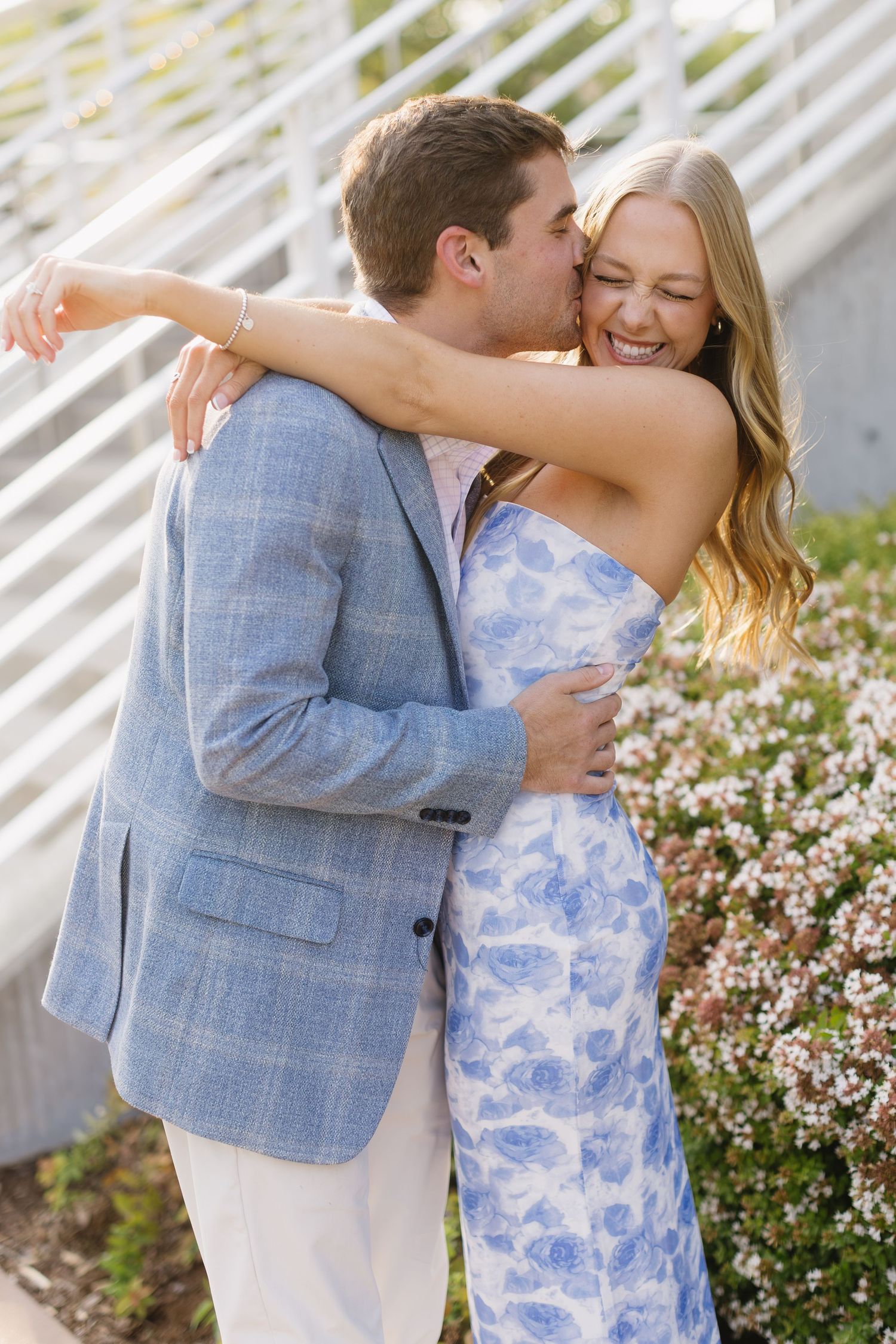 A couple embraces and laughs together outdoors by blooming pink flowers.