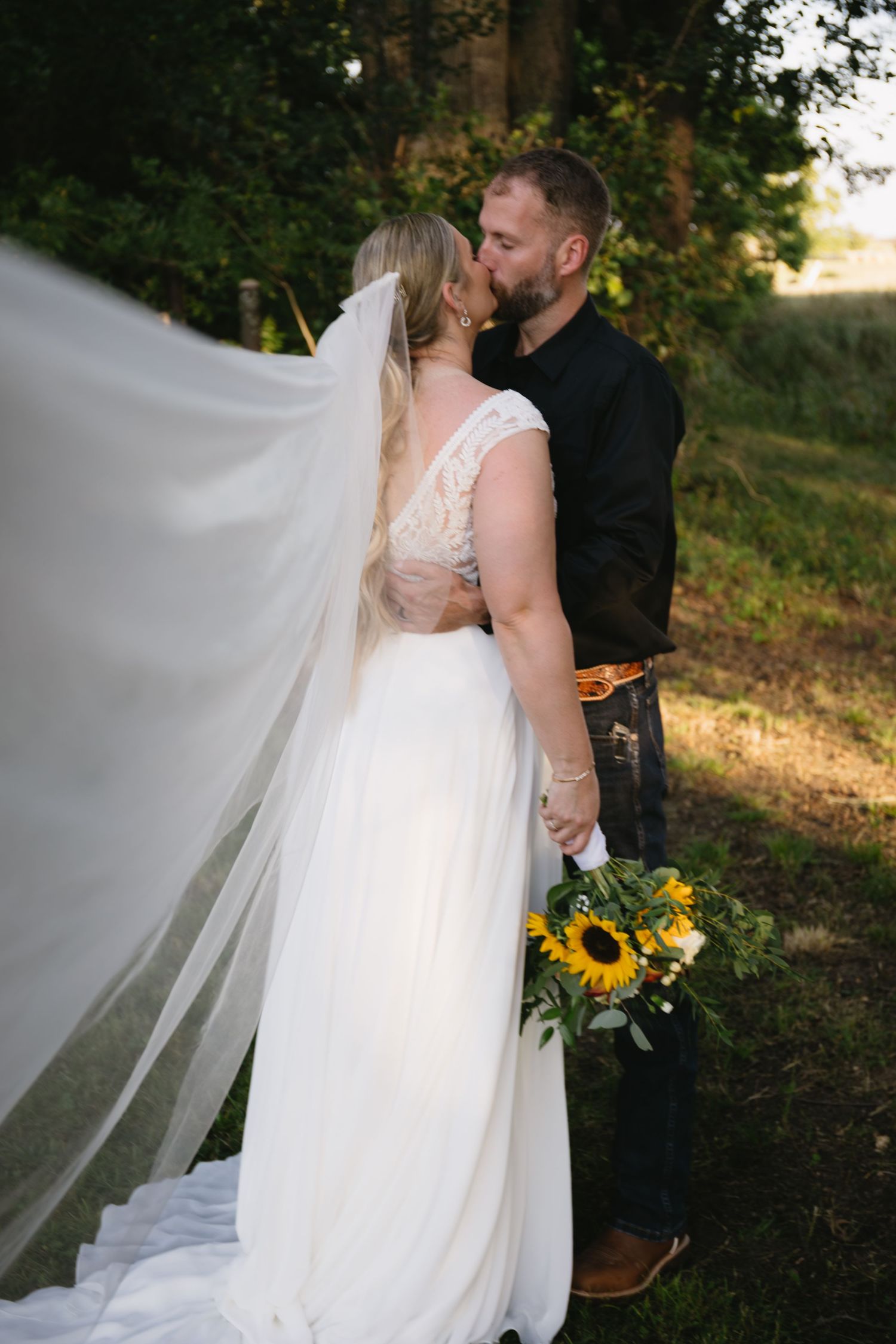 A romantic wedding moment captured with flowing veil and sunflower bouquet against a natural backdrop.