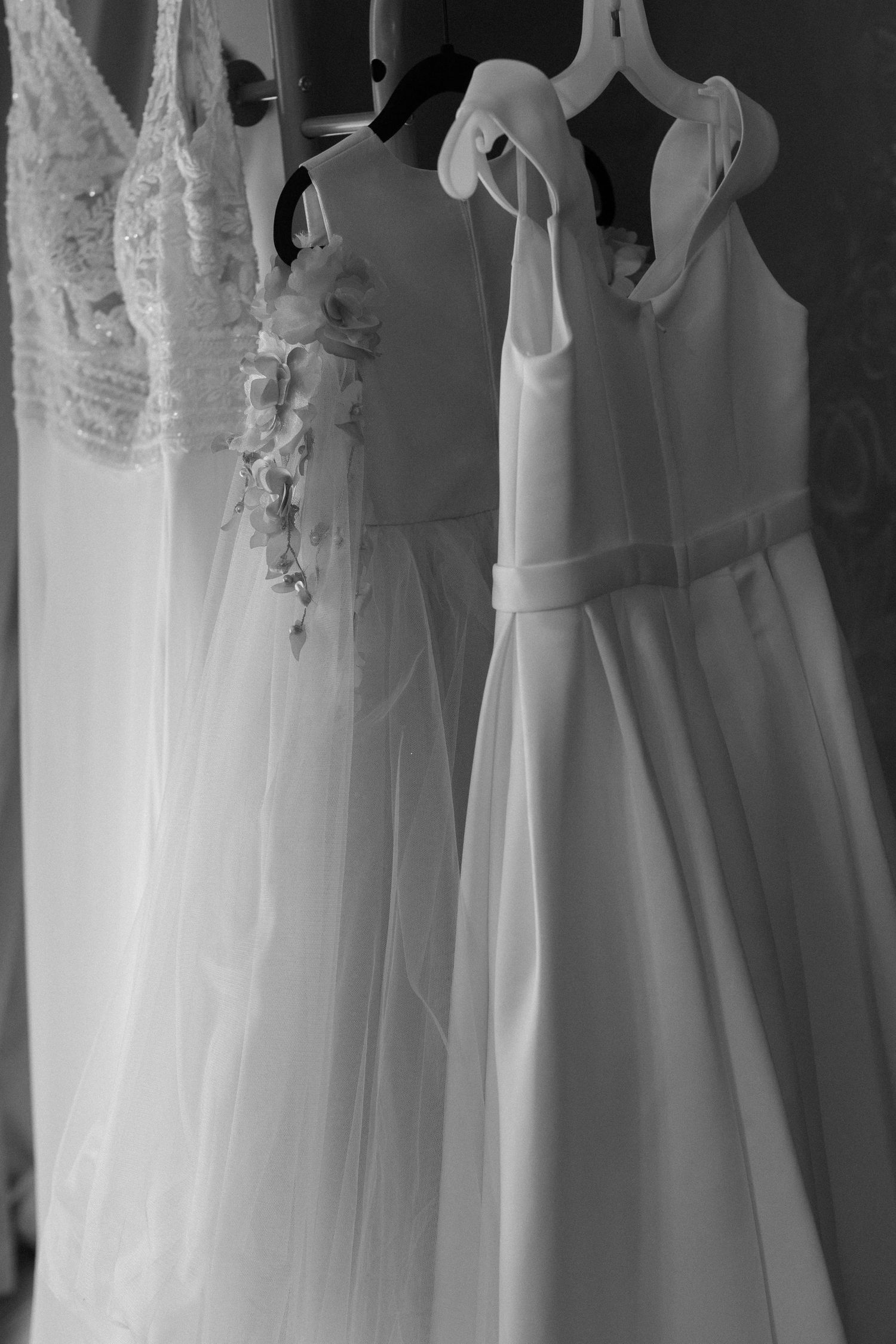 Multiple white wedding dresses hanging on display showing delicate lace and fabric details in black and white.