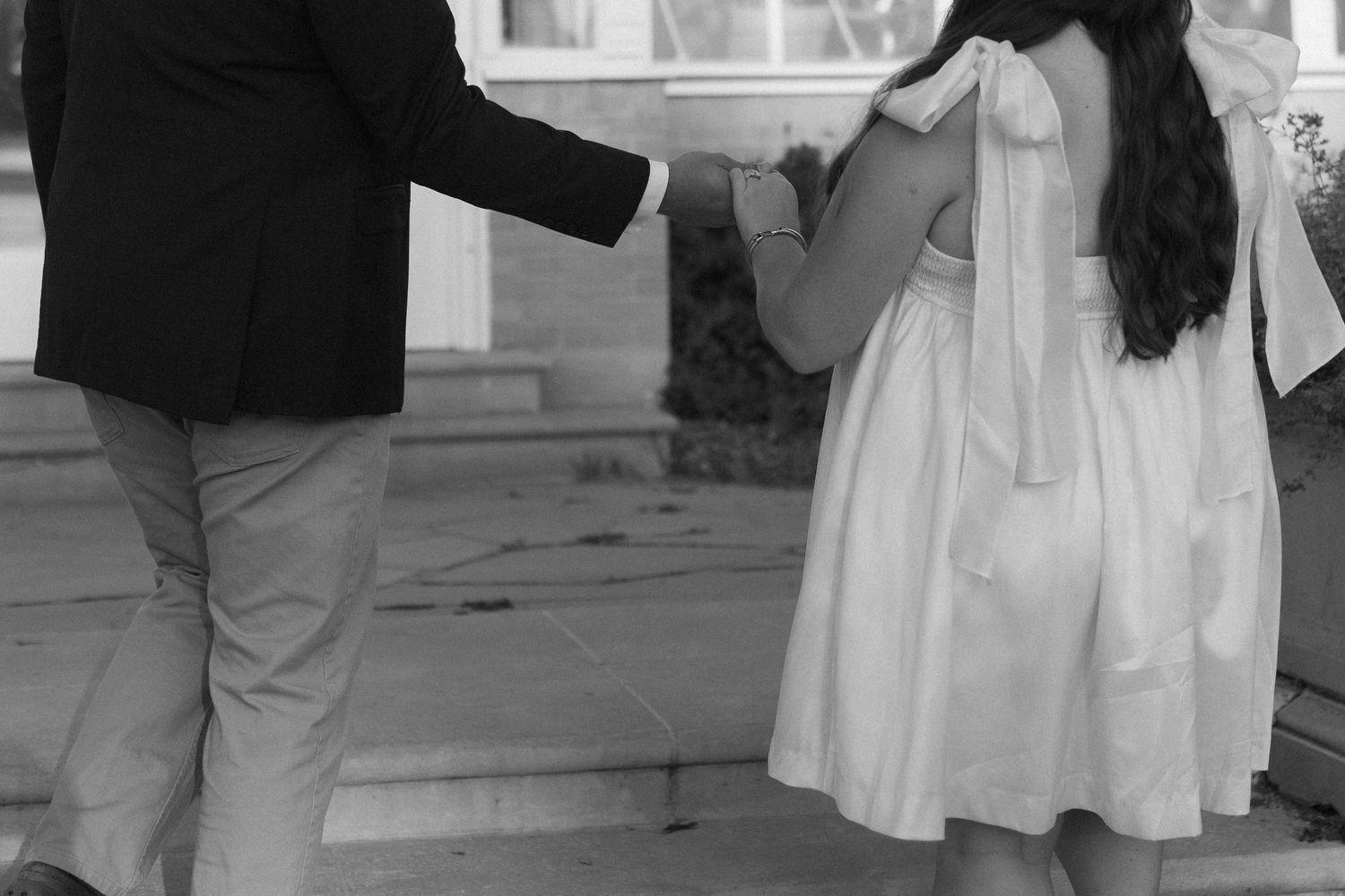 Black and white image showing people in formal attire exchanging a handbag on outdoor steps.