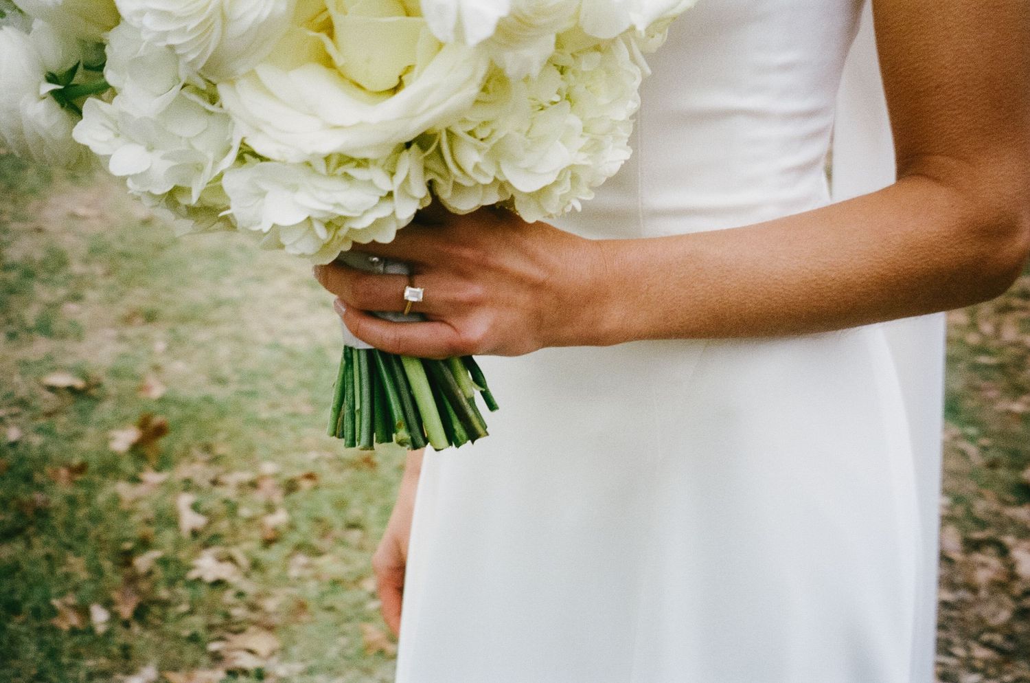 A white hydrangea wedding bouquet held against a simple white wedding dress.