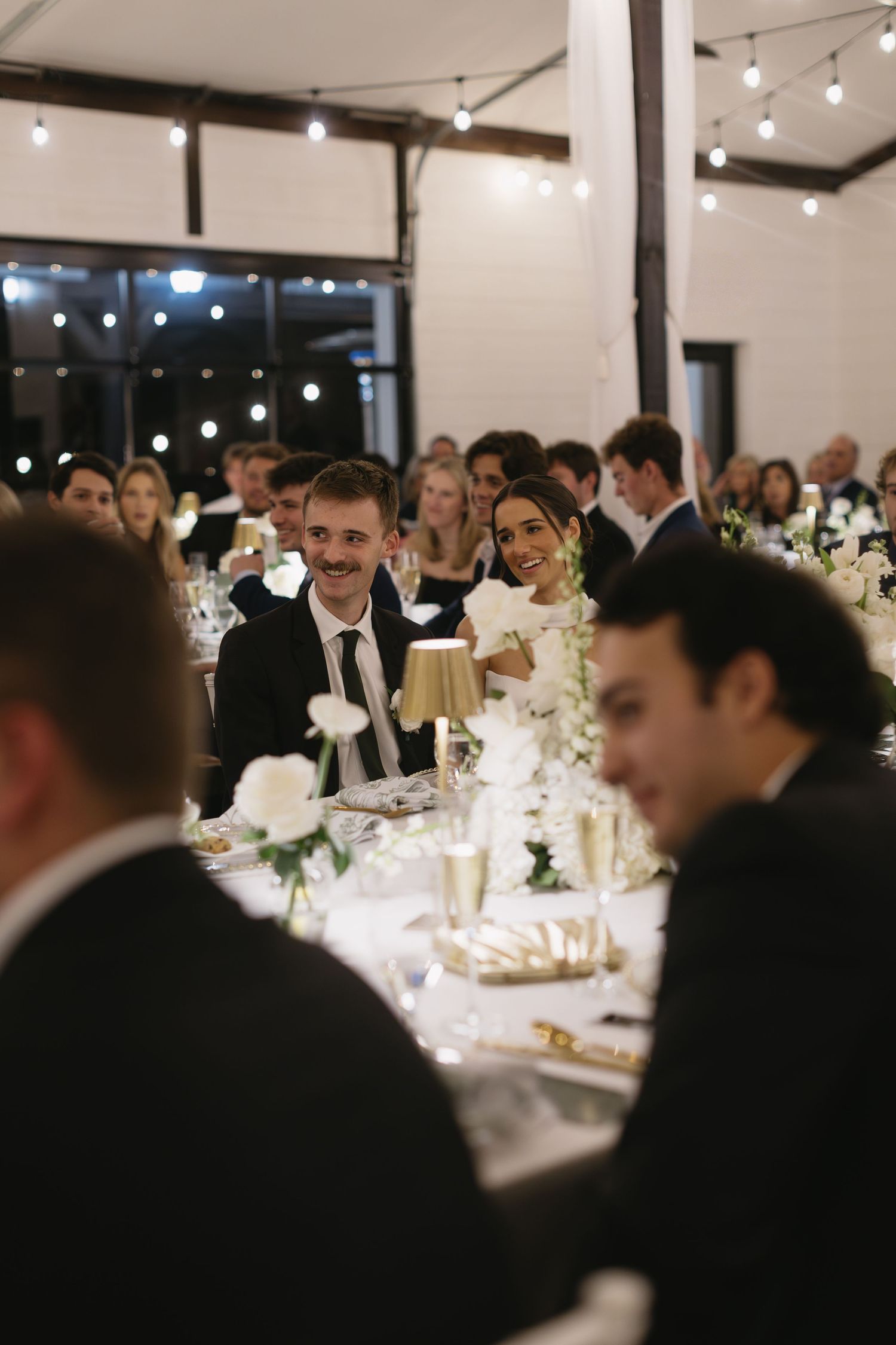 Wedding reception guests seated at elegantly decorated tables in bright modern venue.