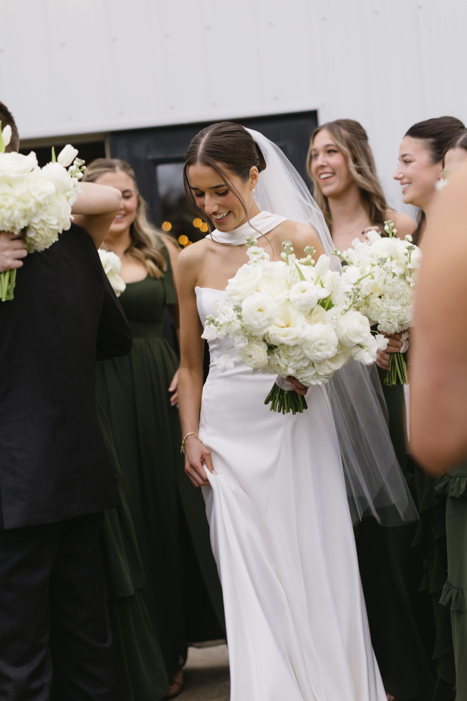 Wedding party members hold white bouquets while wearing black and white formal attire.