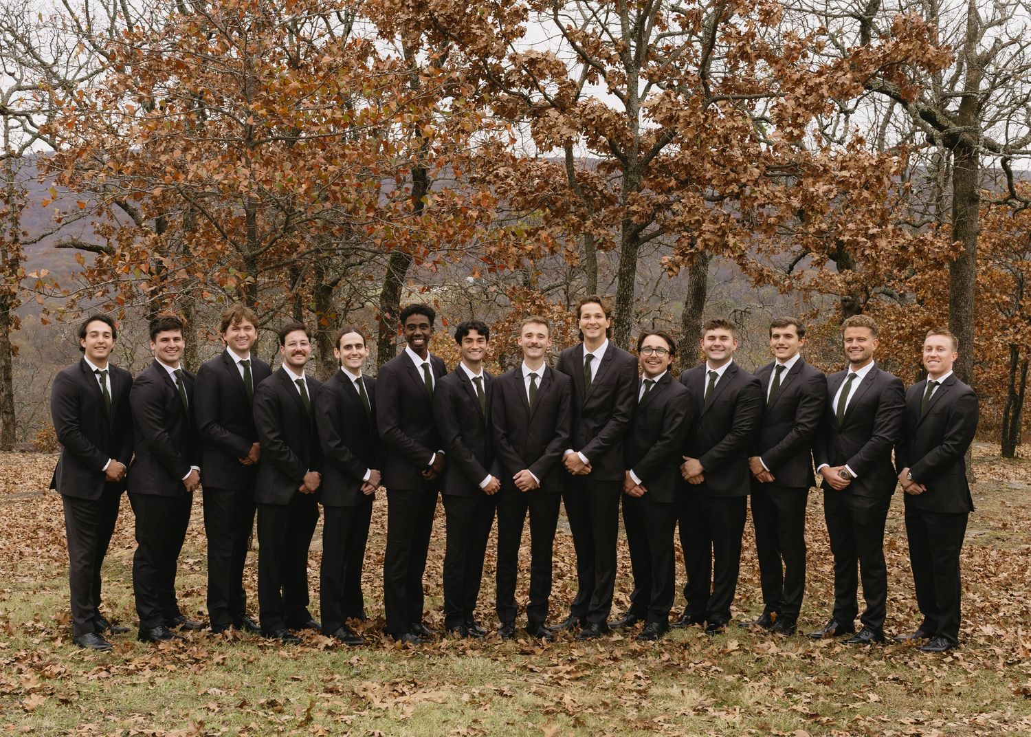Groomsmen in black suits and ties pose in a line during fall wedding photography.