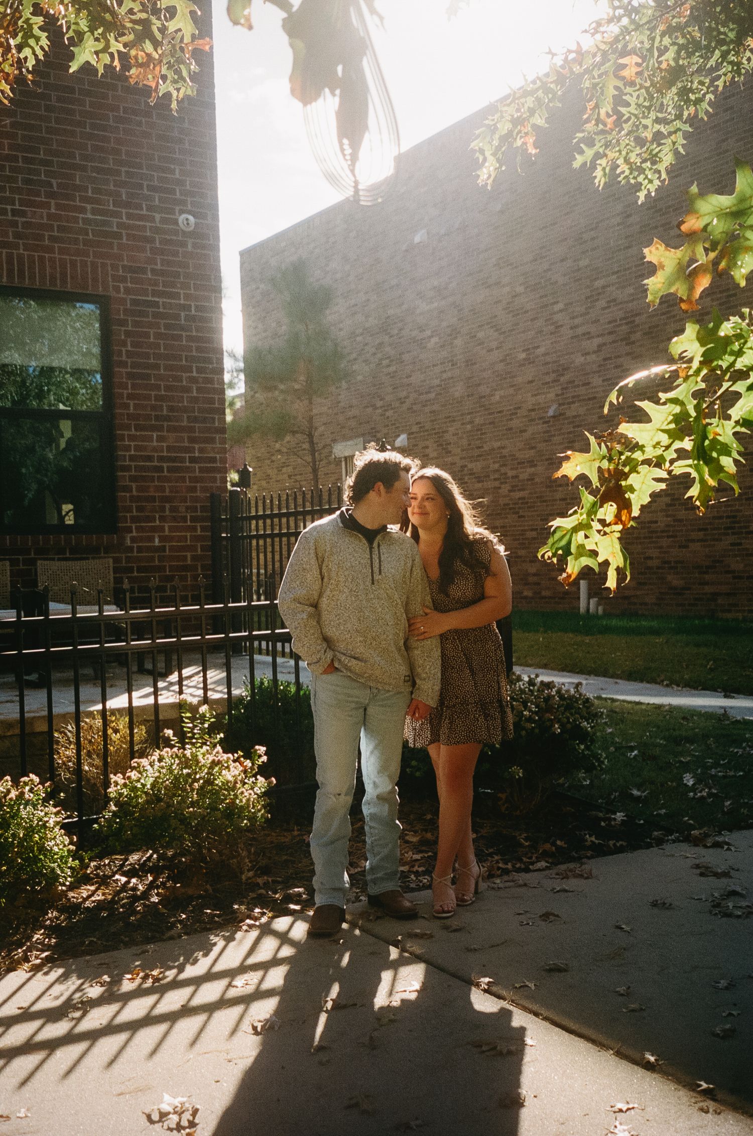 A couple sharing an intimate moment in golden sunlight against a brick wall and garden setting.