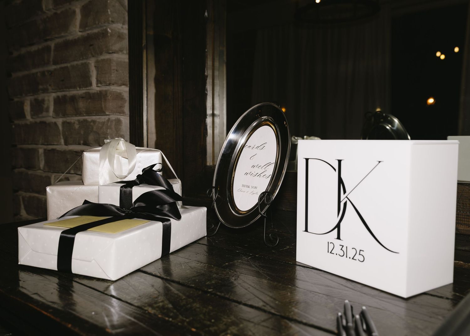 Row of white gift boxes arranged against dark brick wall at wedding venue.