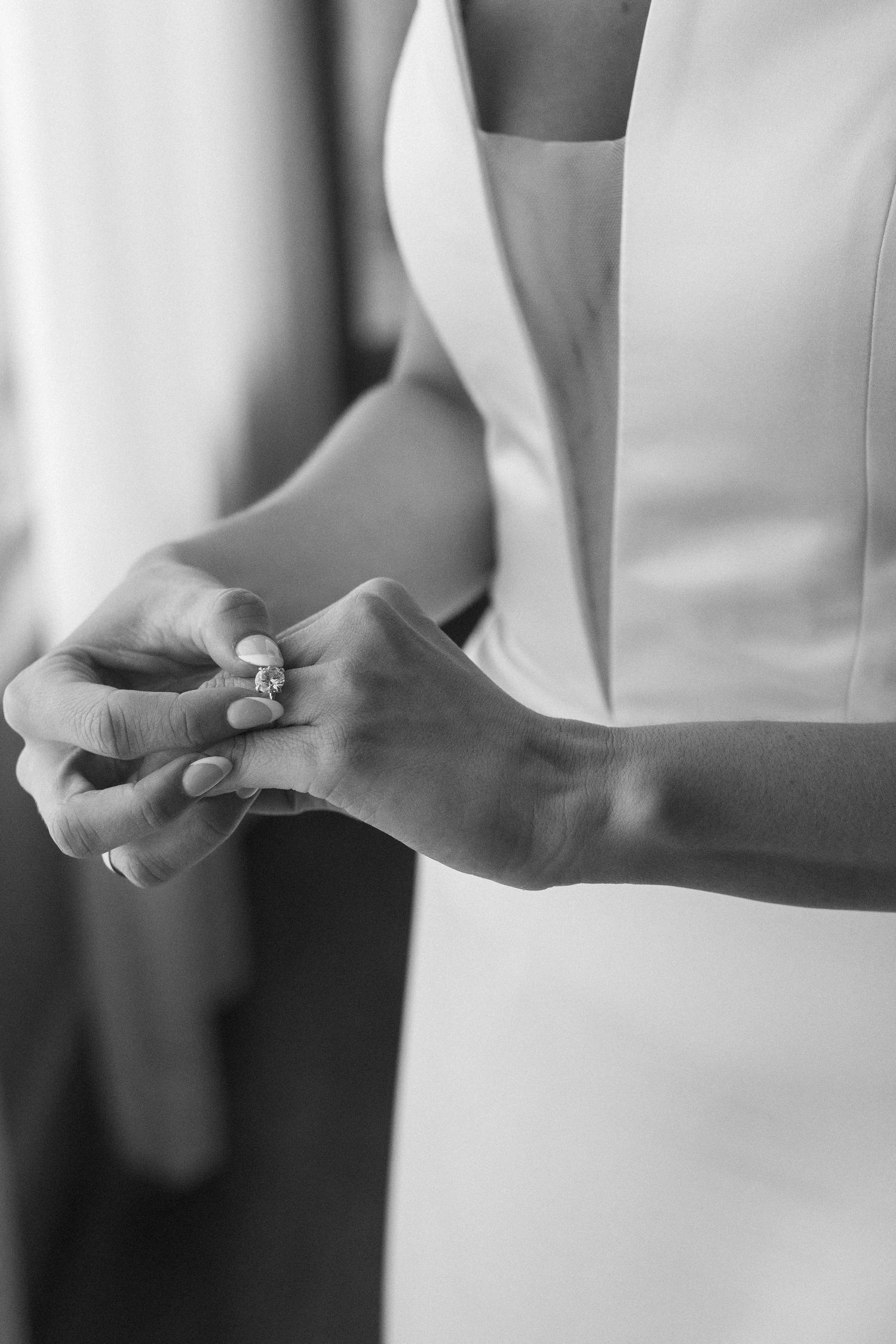 Close-up black and white photo of hands holding a wedding ring against a white background.