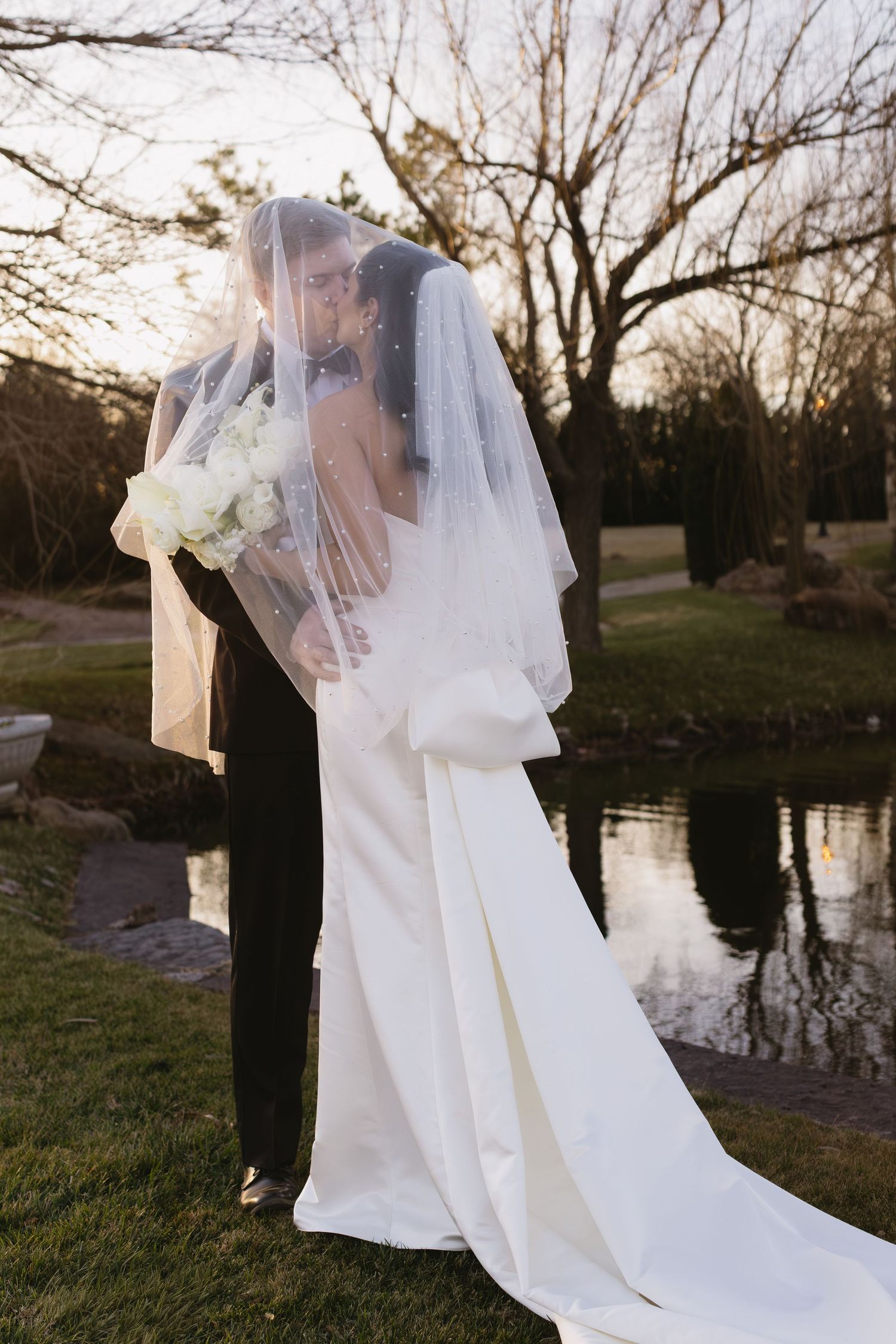 Wedding couple portraits by a reflective pond at sunset with a flowing white veil.