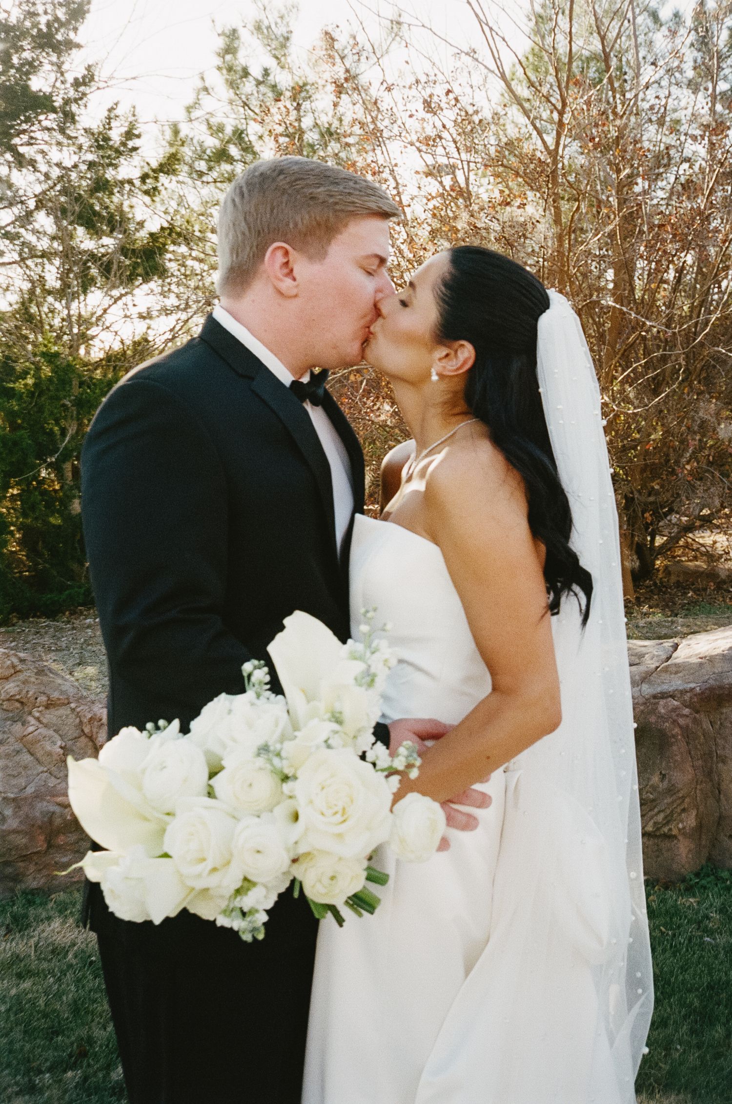 Romantic outdoor wedding portrait with white rose bouquet at sunset.