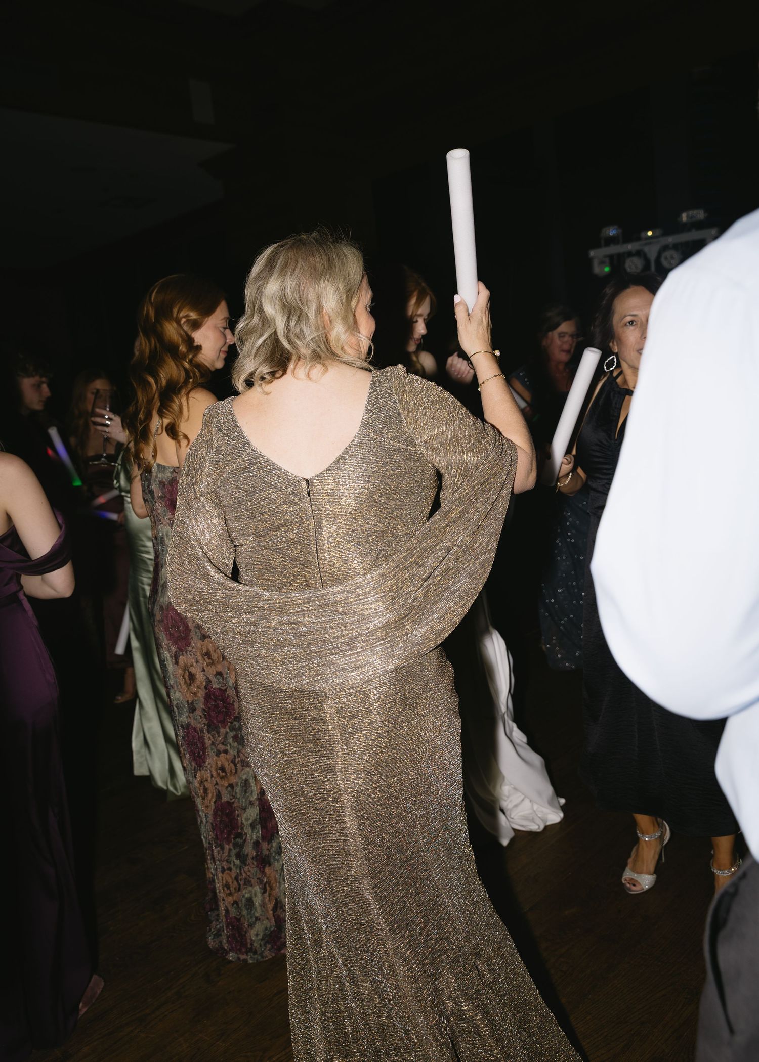 Wedding reception guests dance in sparkly formal attire under dim lighting.