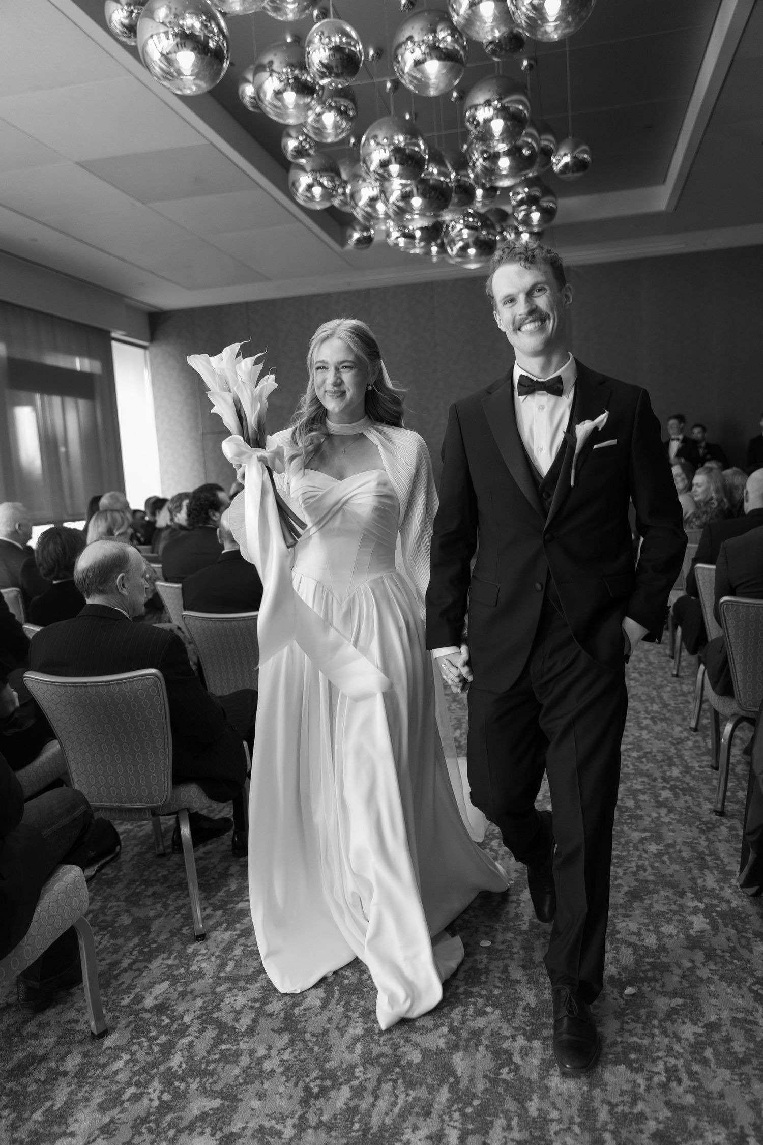 A wedding celebration under silver balloons in an elegant ballroom with patterned carpet.