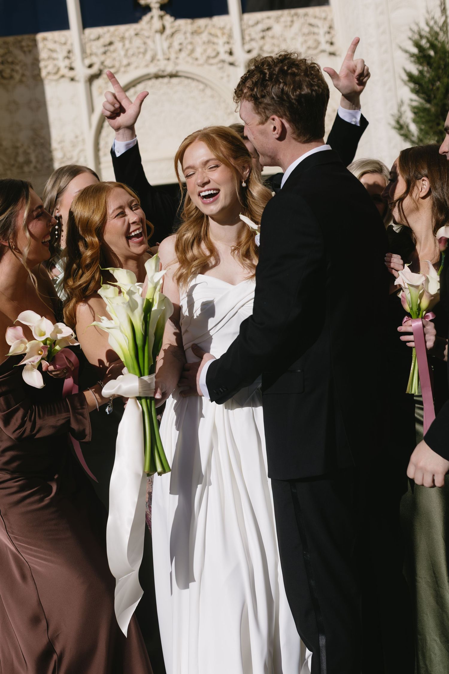 Wedding party celebrating outdoors with bridesmaids in brown dresses and bride in white gown.