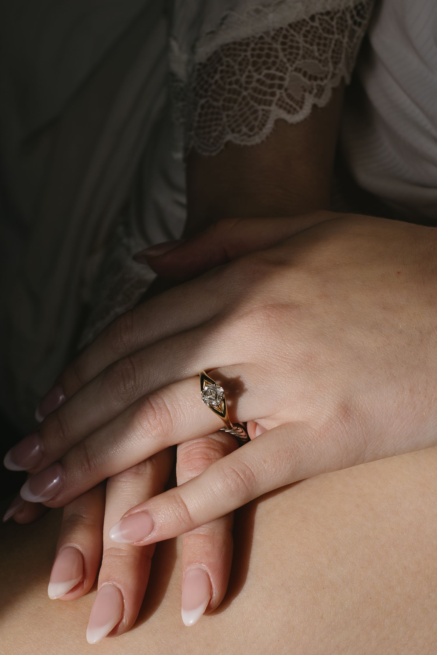 Close-up of hands with engagement ring resting on white lace fabric.