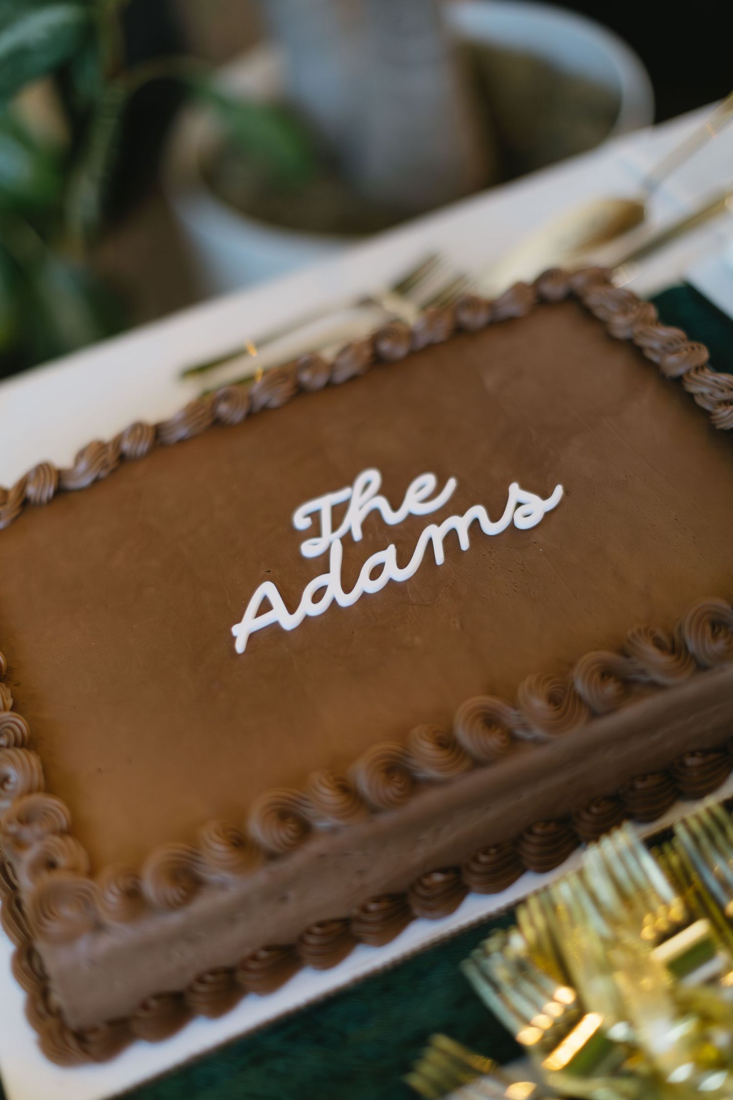 Close-up of chocolate brown wedding cake with white script lettering and piped border details.