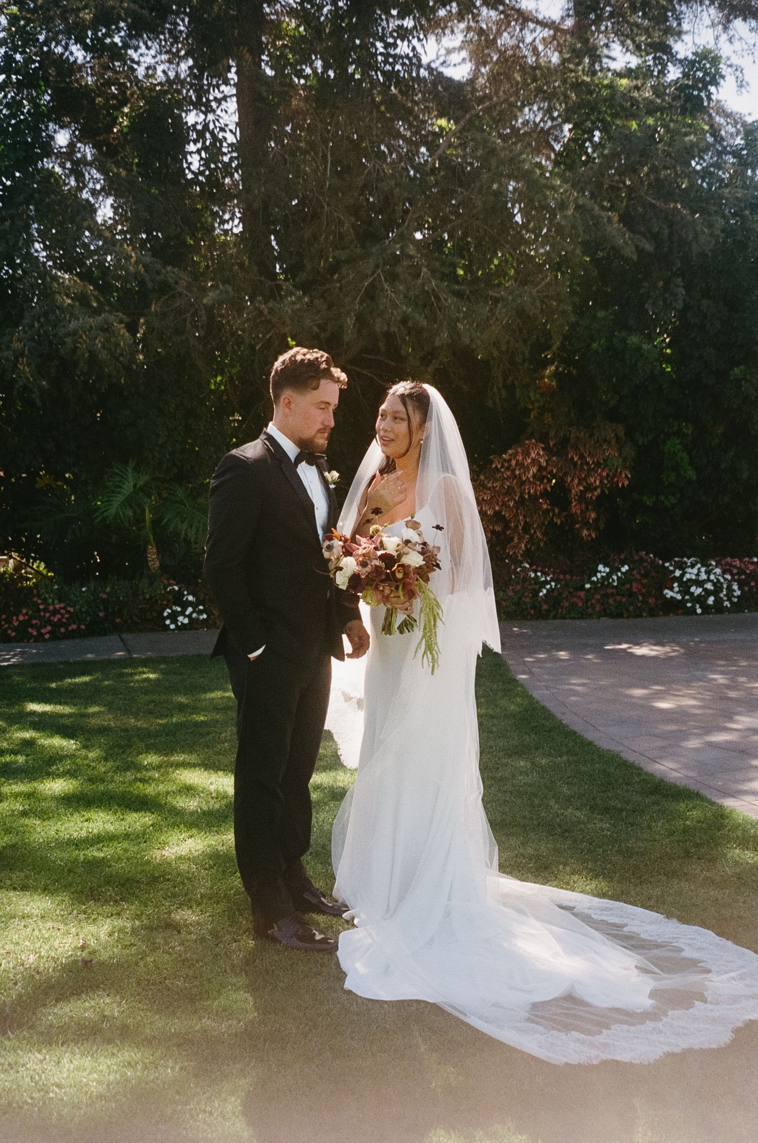 A romantic wedding scene on a manicured lawn with a couple in traditional formal attire and flowing white veil.