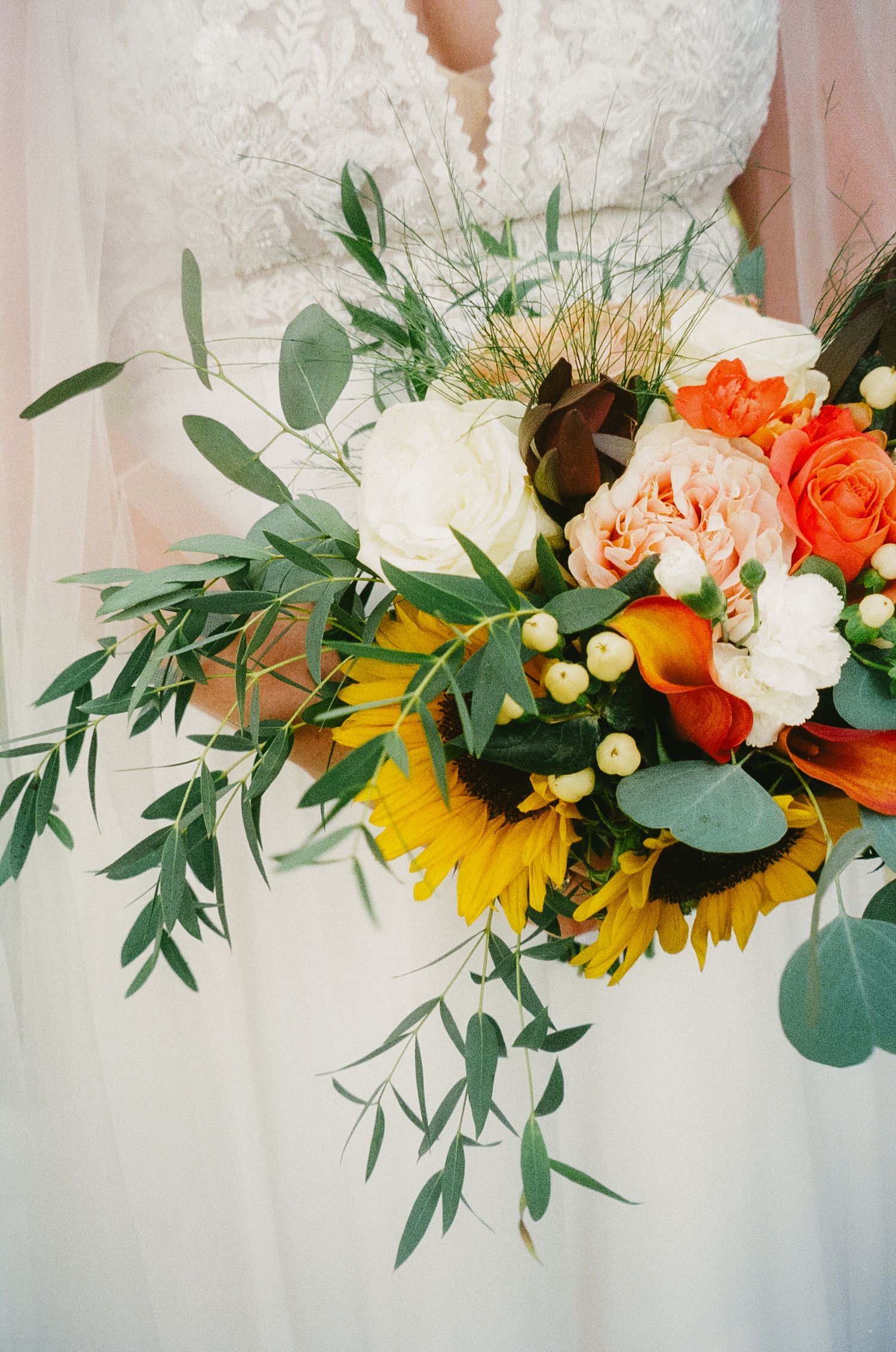 Floral garland with orange roses, yellow sunflowers, white roses and eucalyptus greenery draped along a curtain rod.