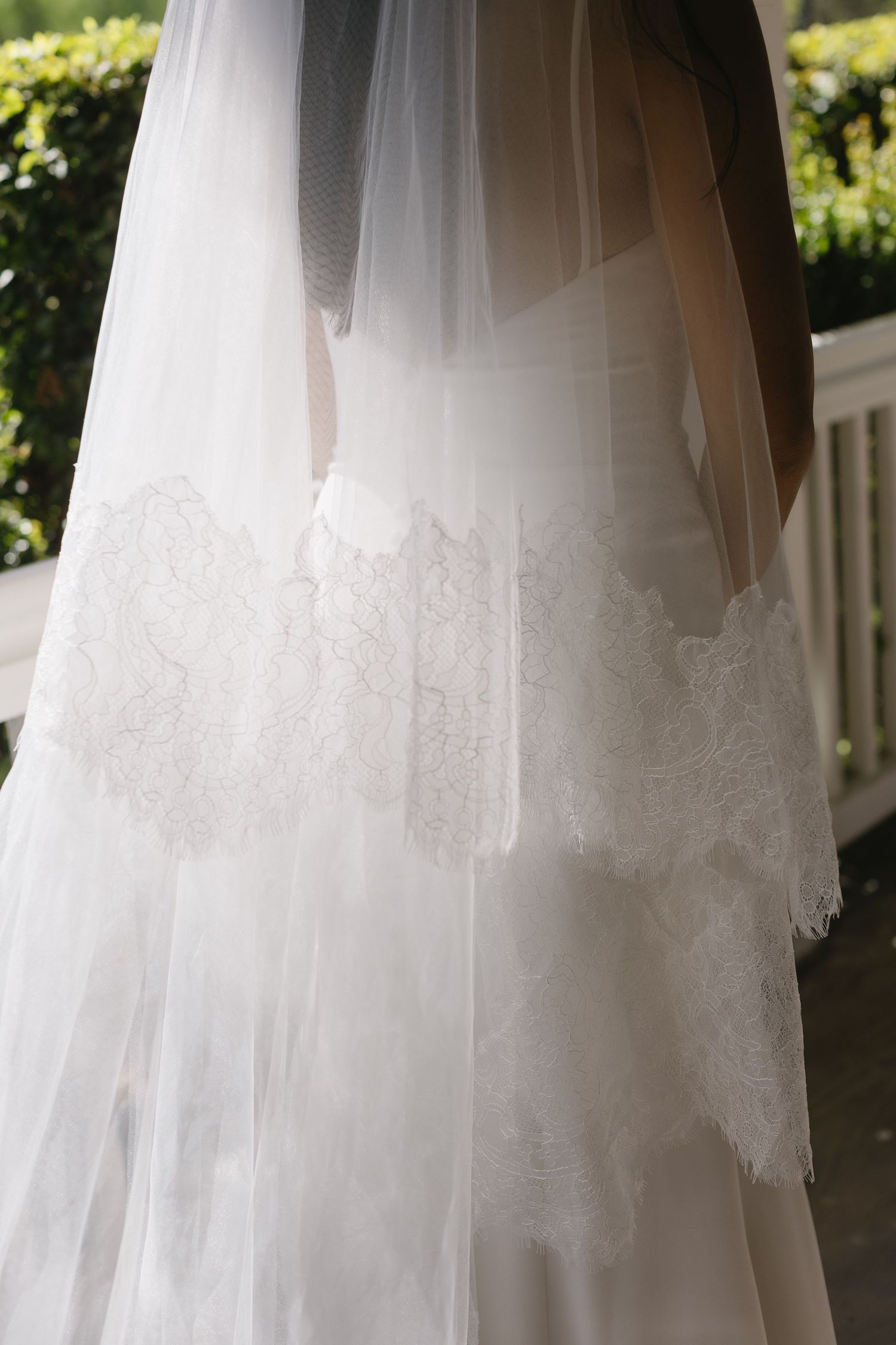 Delicate white lace details on a flowing wedding dress veil captured in natural sunlight.